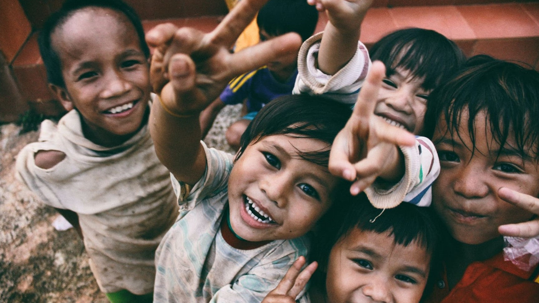 Happy children laughing and showing peace signs while playing together outdoors.