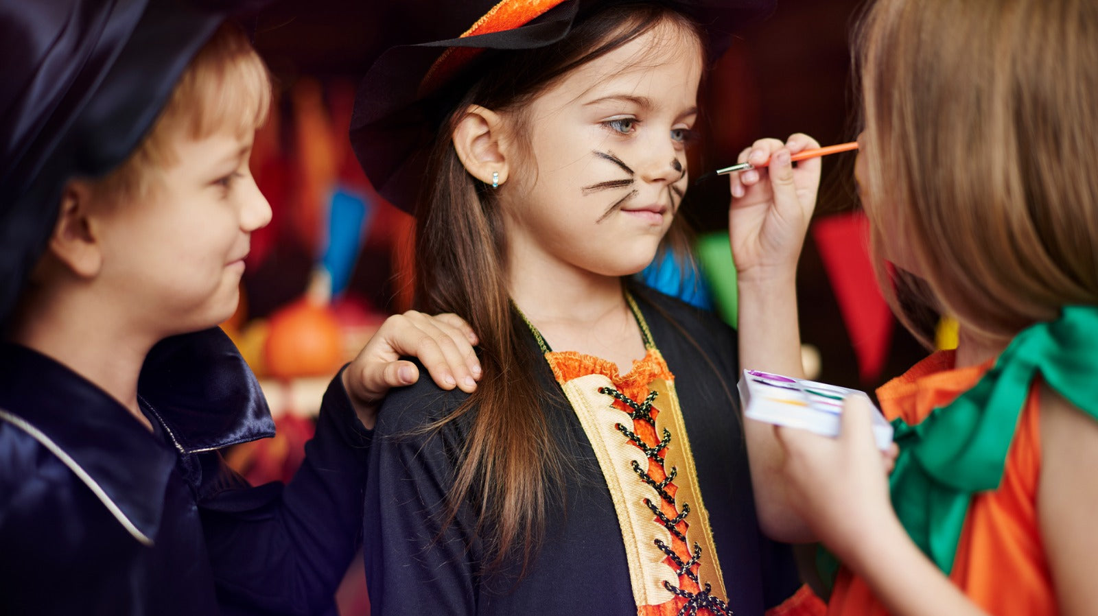 Children in Halloween costumes enjoying face painting activity during a festive party.