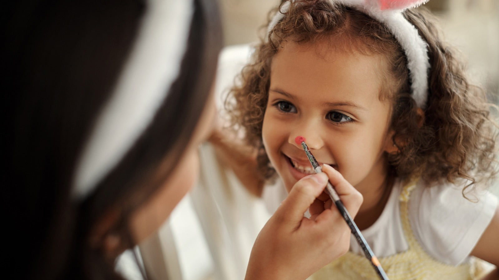 Child in bunny ears enjoying face painting activity at a fun event.