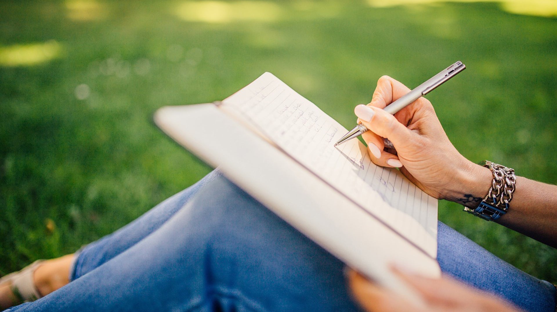 Close-up of a person journaling in a notebook while relaxing in a park.