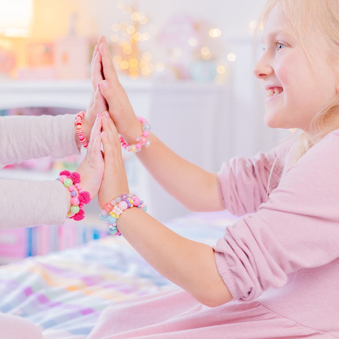 Two young girls in pink shirts give each other a high-five. They both wear colorful beaded bracelets.