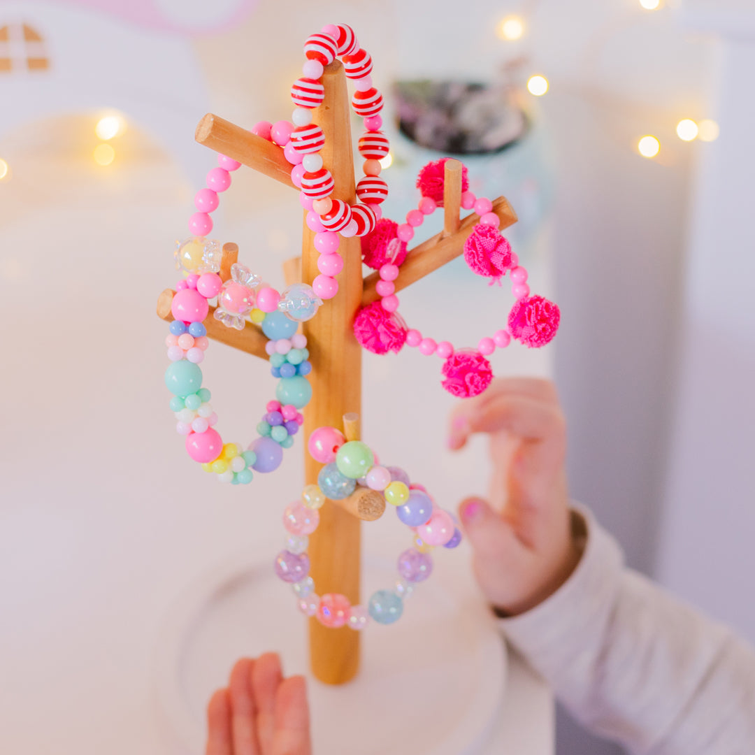 Wooden jewelry tree stand with colorful beaded bracelets. Child's hand in frame.