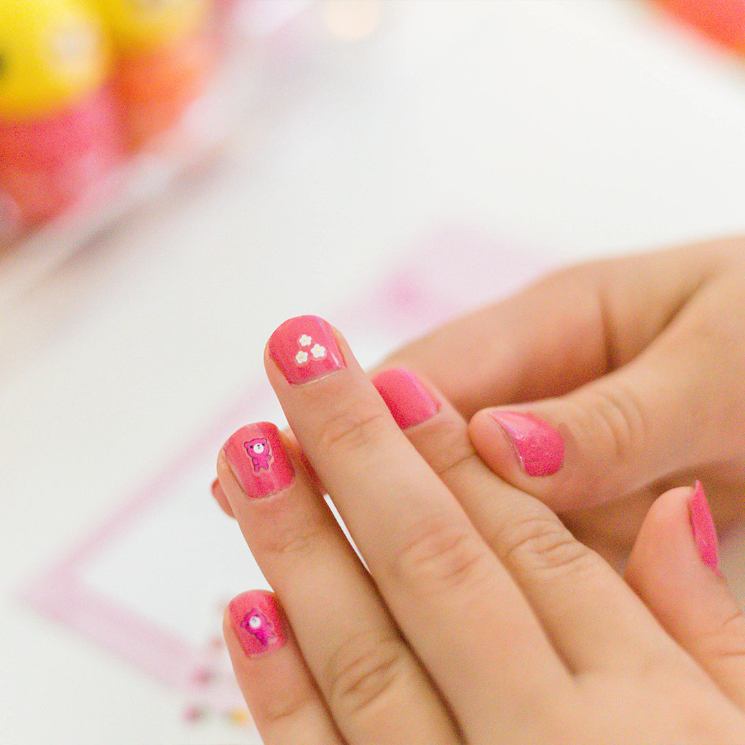 Close-up of pink manicured nails with cartoon designs on fingers.