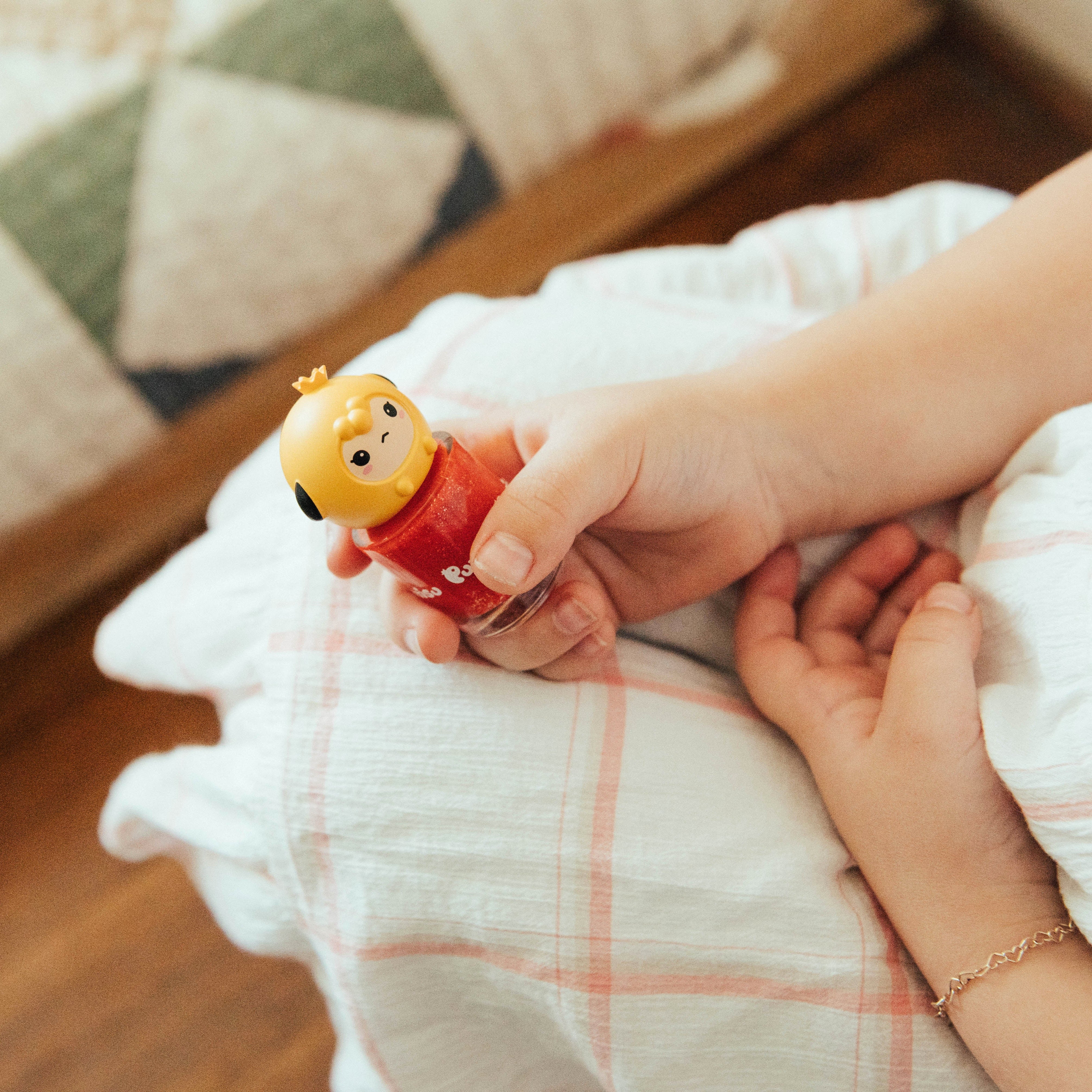 Child's hand holding red glitter nail polish with a yellow toy top.