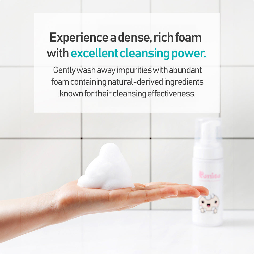 Hand holding a mound of white cleansing foam in a white-tiled bathroom, next to a bottle of "Ponisa" face wash.