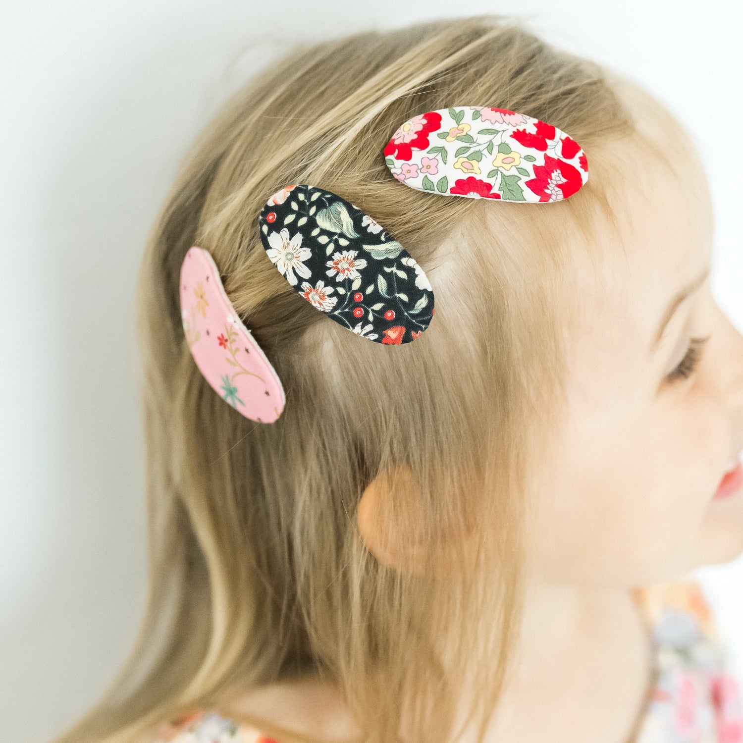 Colorful oval shape floral pattern hair clips on a kid's head with a plain background