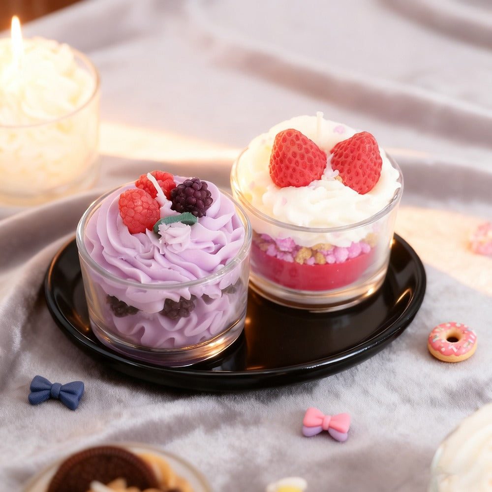 Two small glass desserts cupcake candles with whipped cream and berries on a black plate, surrounded by decorative items.