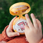 Hands holding a yellow makeup compact with a pink bear.