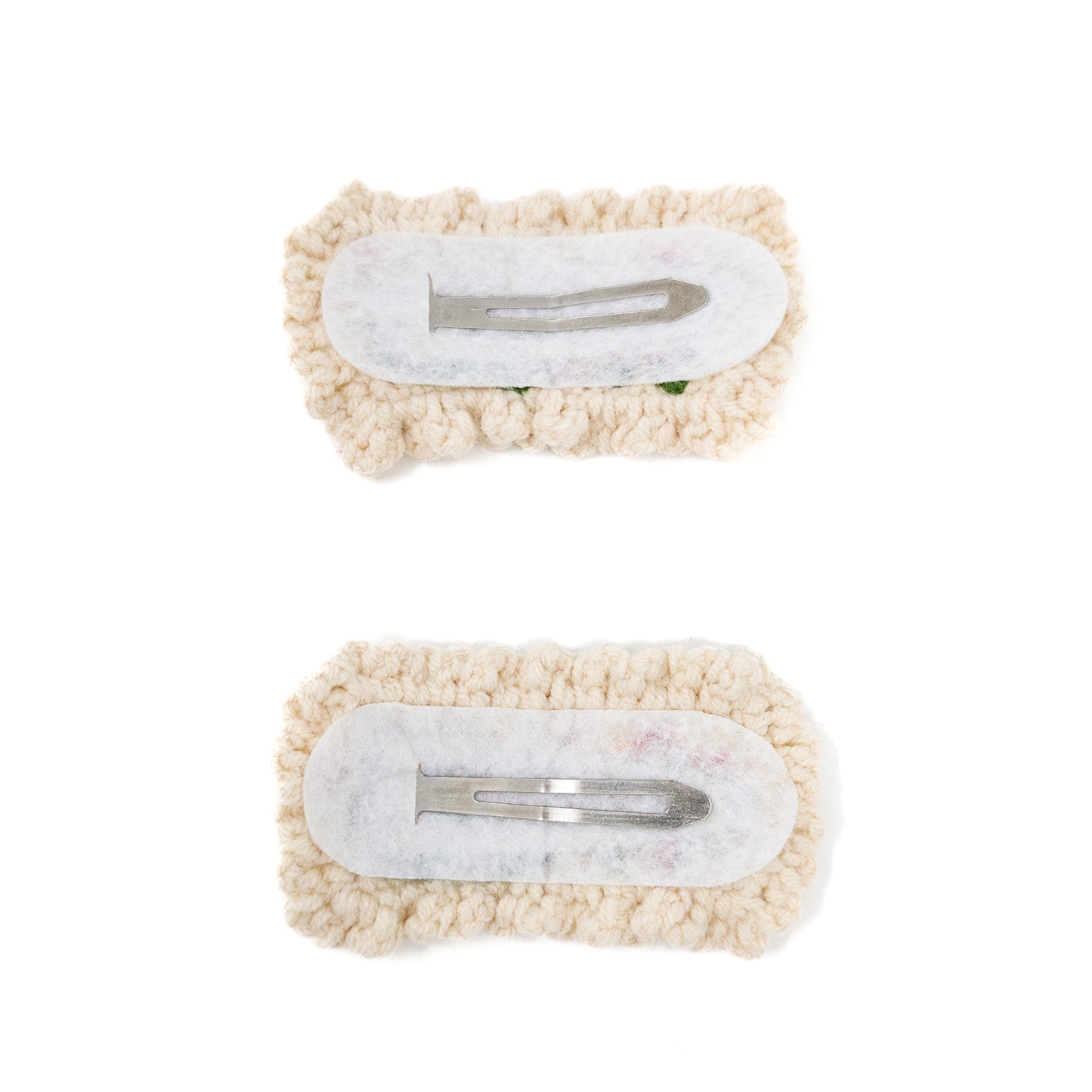 Two handmade, knitted hair clips on white background.