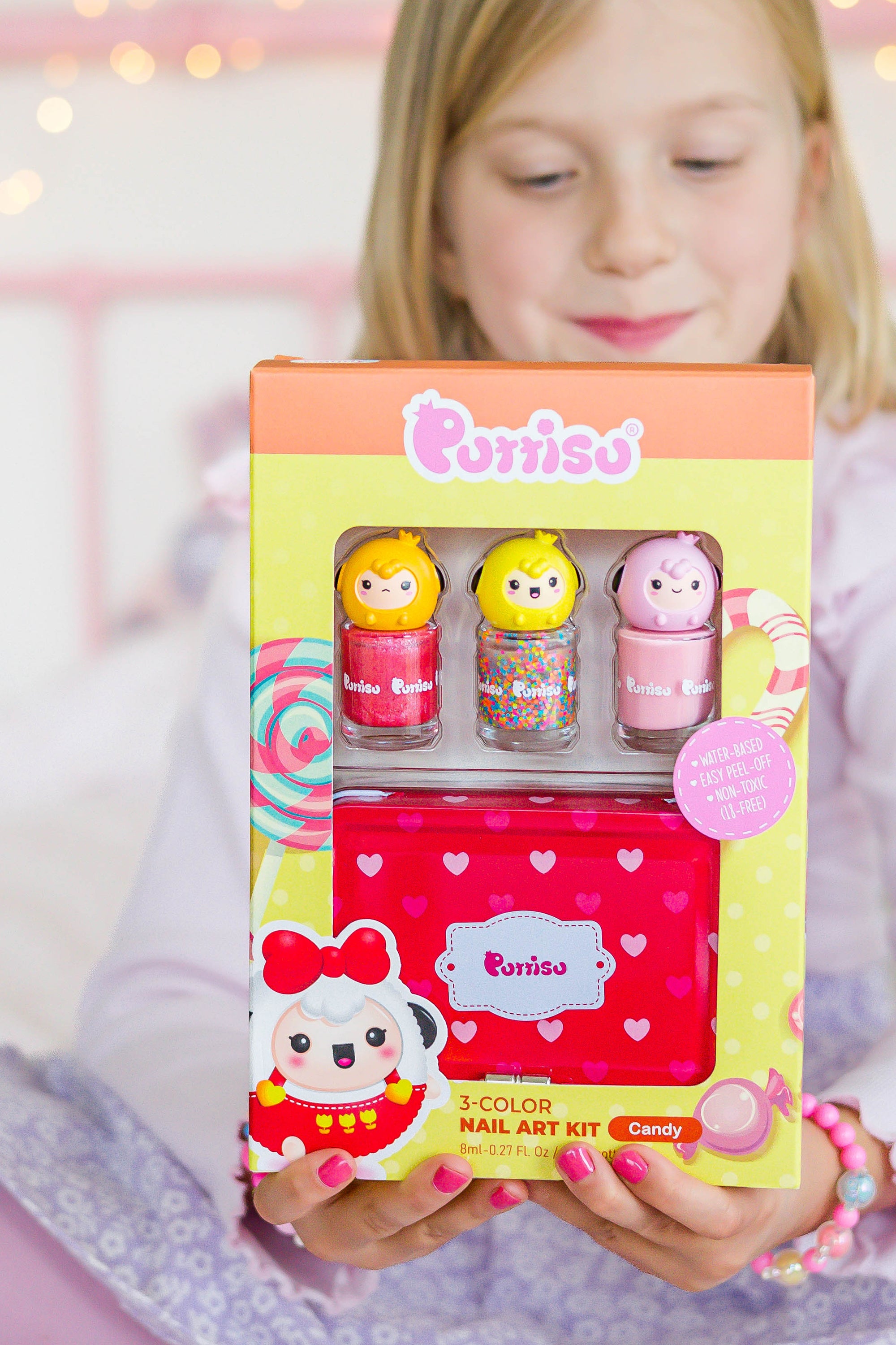 Young girl holds a colorful "Purriso" nail art kit with three polishes and a red heart-patterned tin.