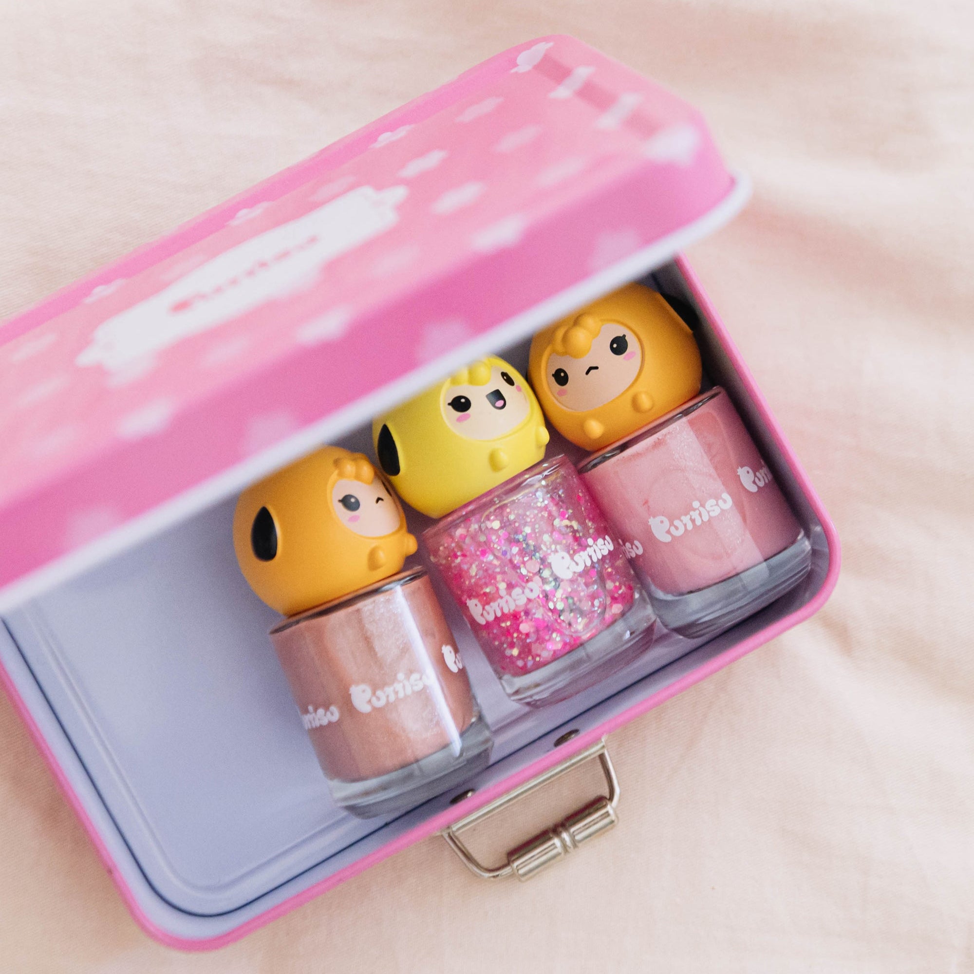 A set of three colorful nail polishes in a pink and white metal box.