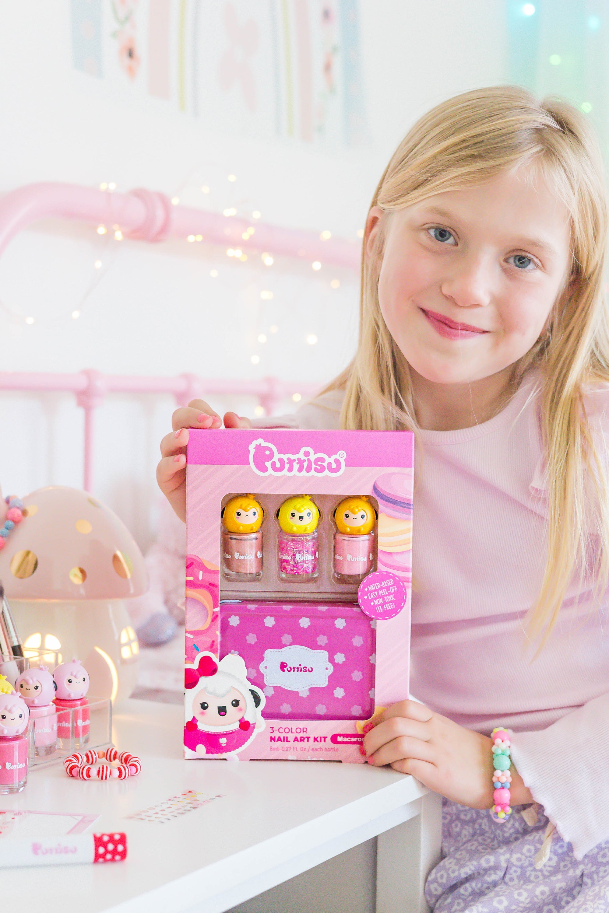 A blonde girl in pink clothes holds a Purriso nail art kit.