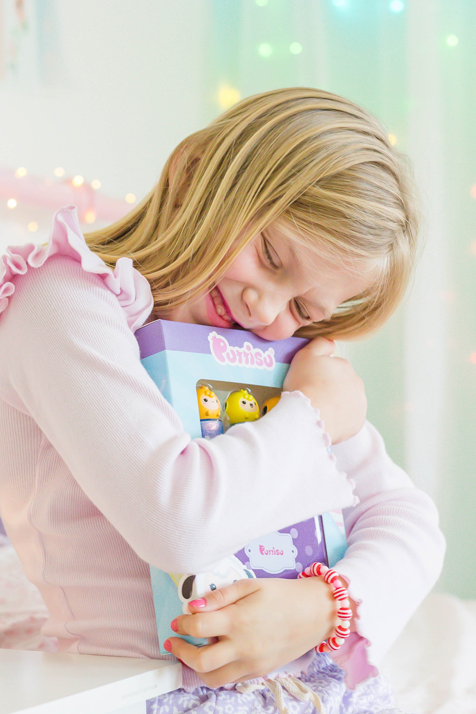 A young girl in a pink shirt and bracelet embraces a Purriso toy box.