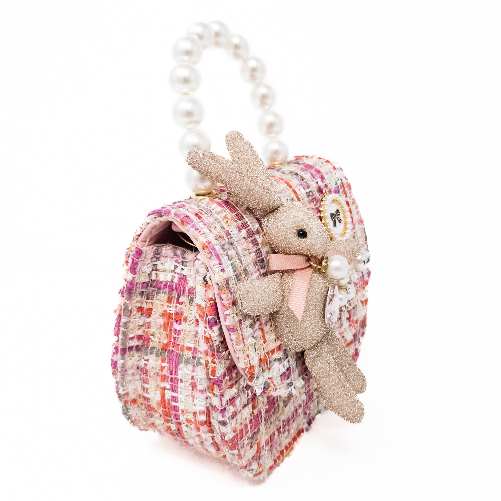 Close-up of a small, pink, tweed purse with a bunny attached, a pearl handle, and a white background.