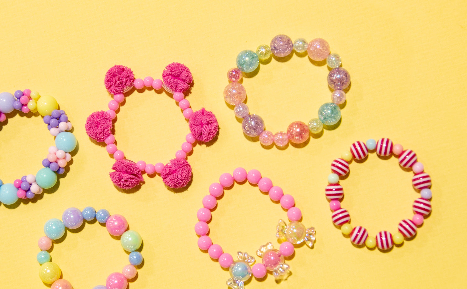 Puttisu kids bead bangles in colorful designs with pom-poms, candy beads, and pastel pearls arranged on a yellow background.