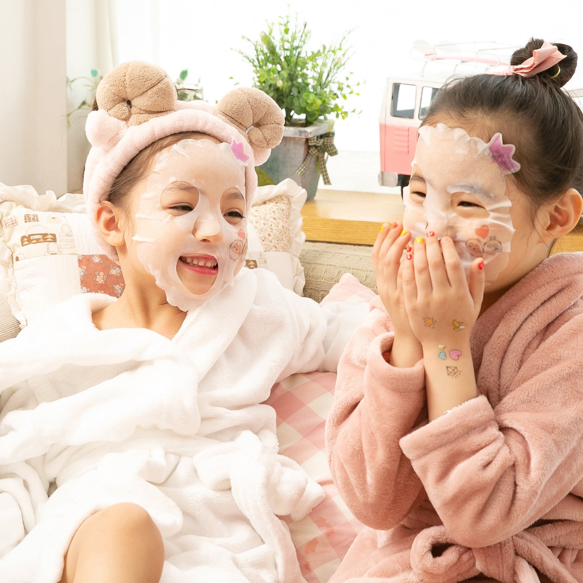 Two girls in robes and face masks laughing indoors.