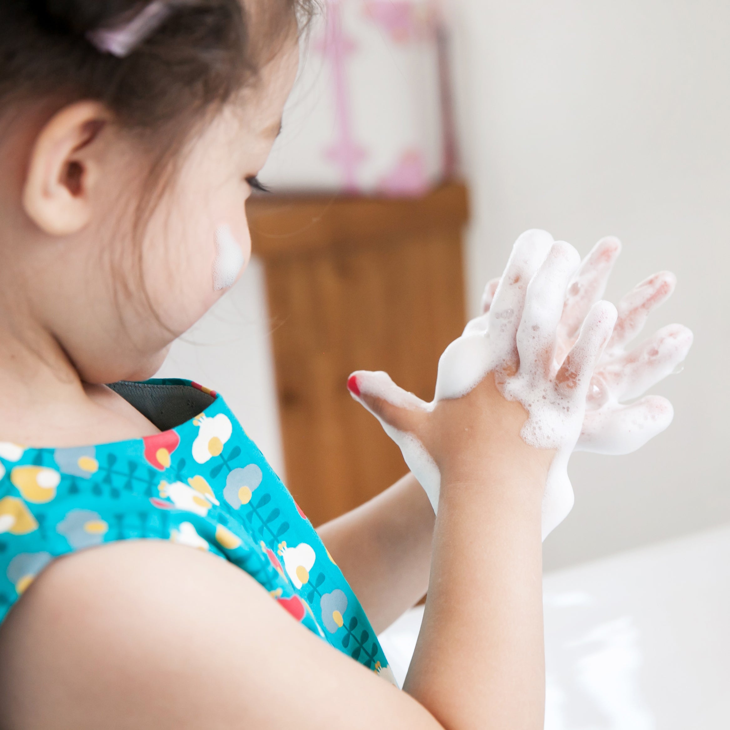 A child with soapy hands in a bathroom.