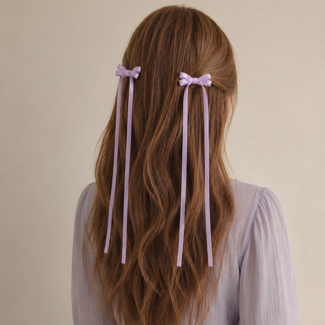 Lavender ribbon bow clip set with long tails, styled in wavy brown hair, seen from the back.