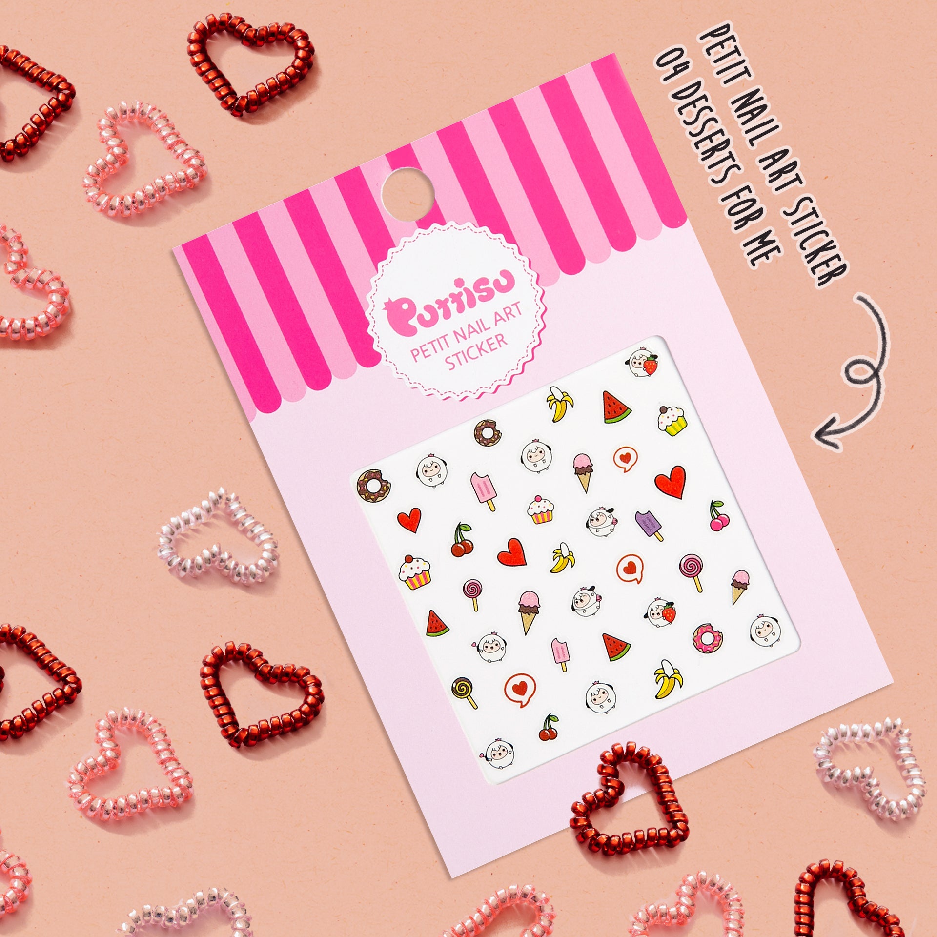 Close-up shot of nail art sticker sheet with dessert-themed designs, surrounded by heart-shaped coiled hair ties in red and pink on a light pink background.
