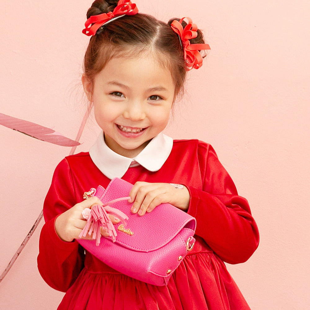 Smiling girl in a red dress with a white collar, holding a pink purse.
