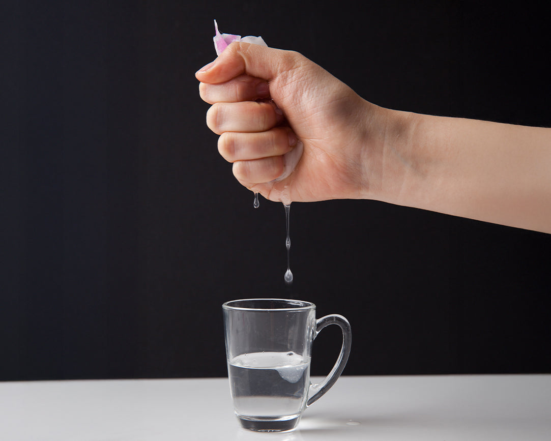 Hand pouring Puttisu real fruit sheet mask essence liquid into a clear glass of water on a black background