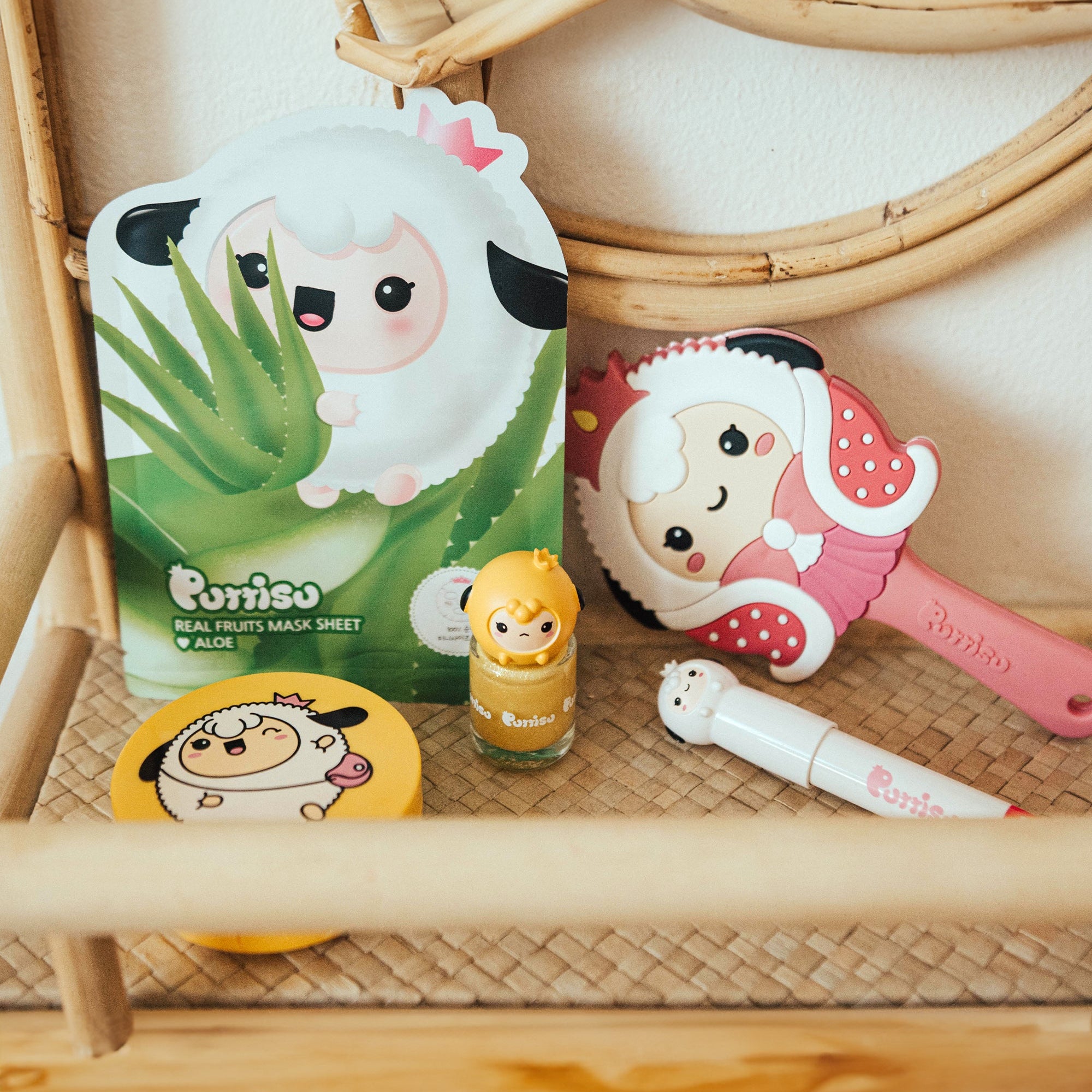 Close-up of Purriso-brand skincare and beauty products, including a sheet mask, a nail polish with a sheep figure on top, a round container with a sheep illustration, a brush with a sheep design, and a lip balm. The products are placed on a woven shelf of a light-colored wooden frame.