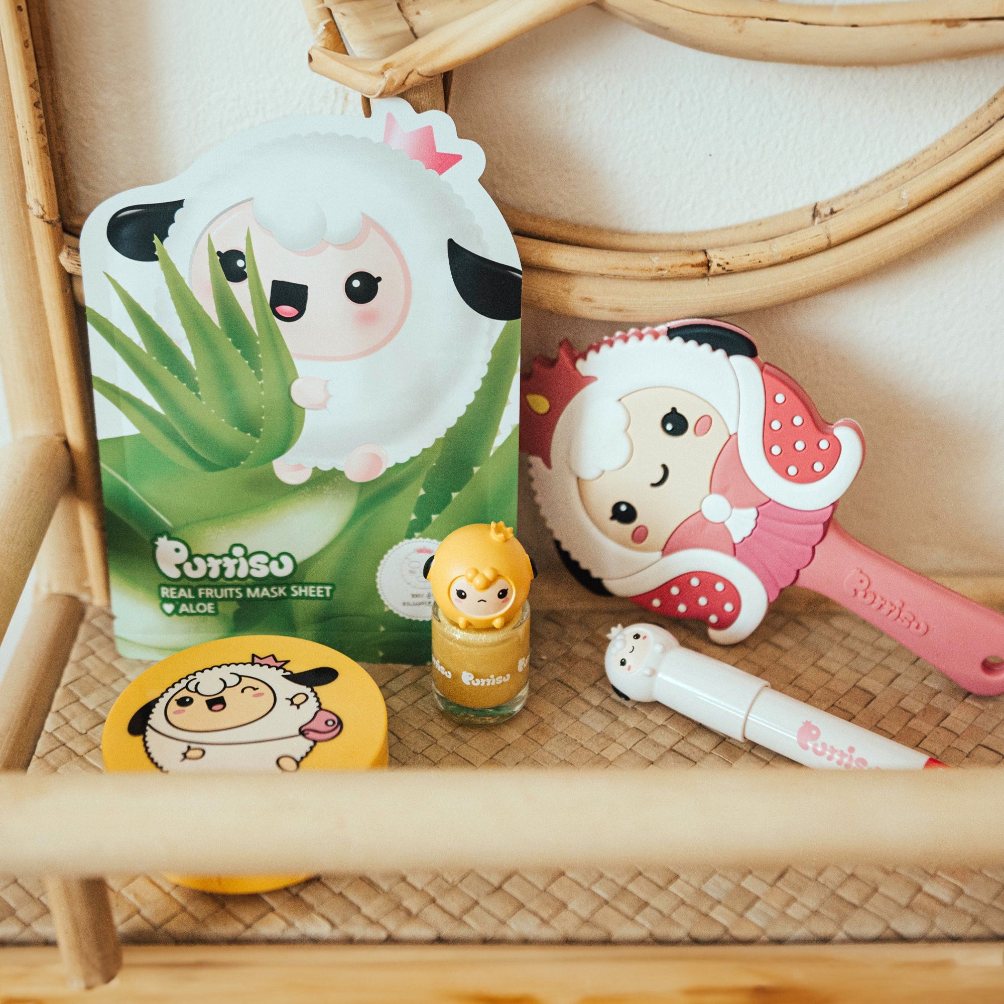 Close-up shot of skincare products on a woven shelf: sheet mask with aloe and a cartoon sheep, a yellow nail polish, a pink brush and a white applicator.