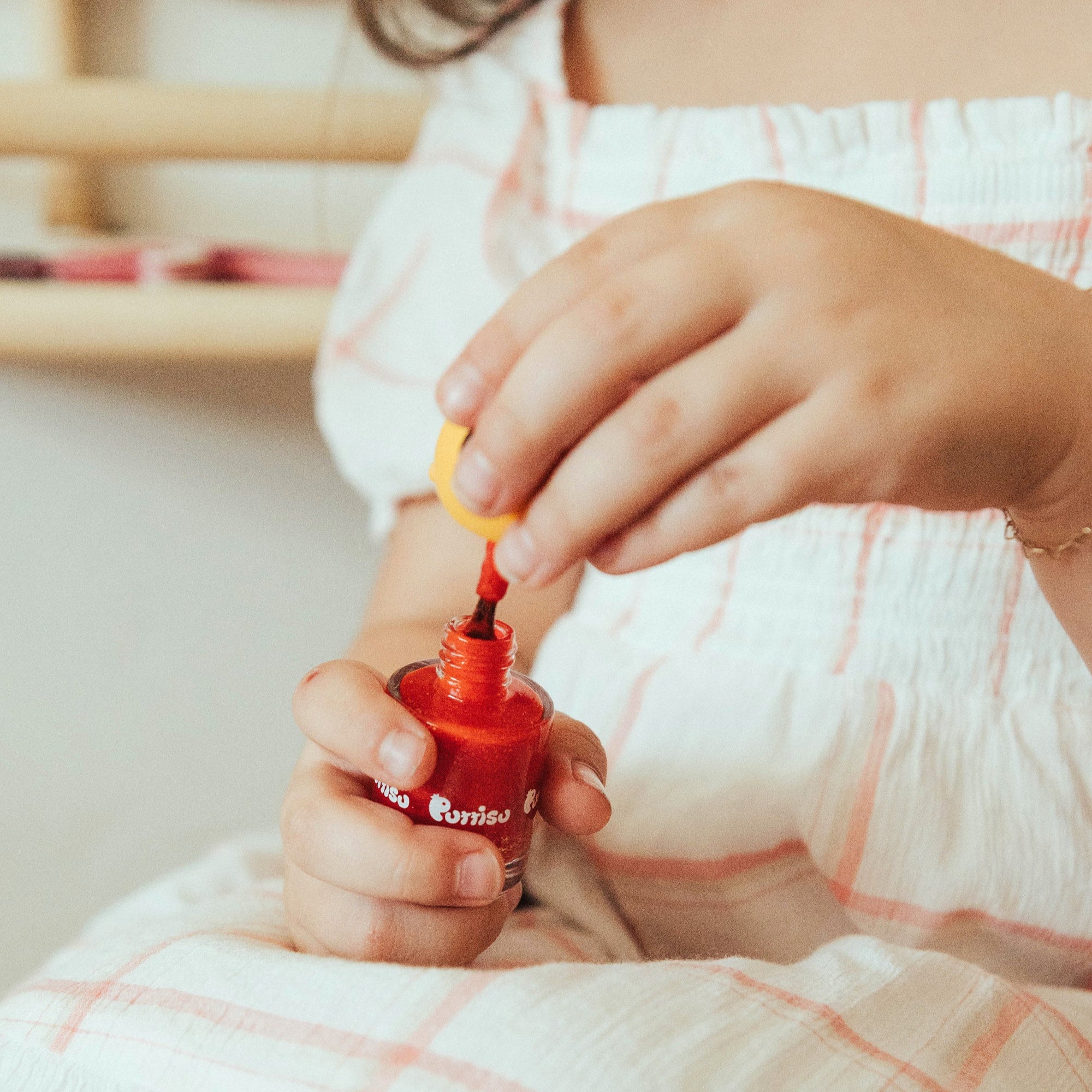 Child in plaid dress holding red nail polish.