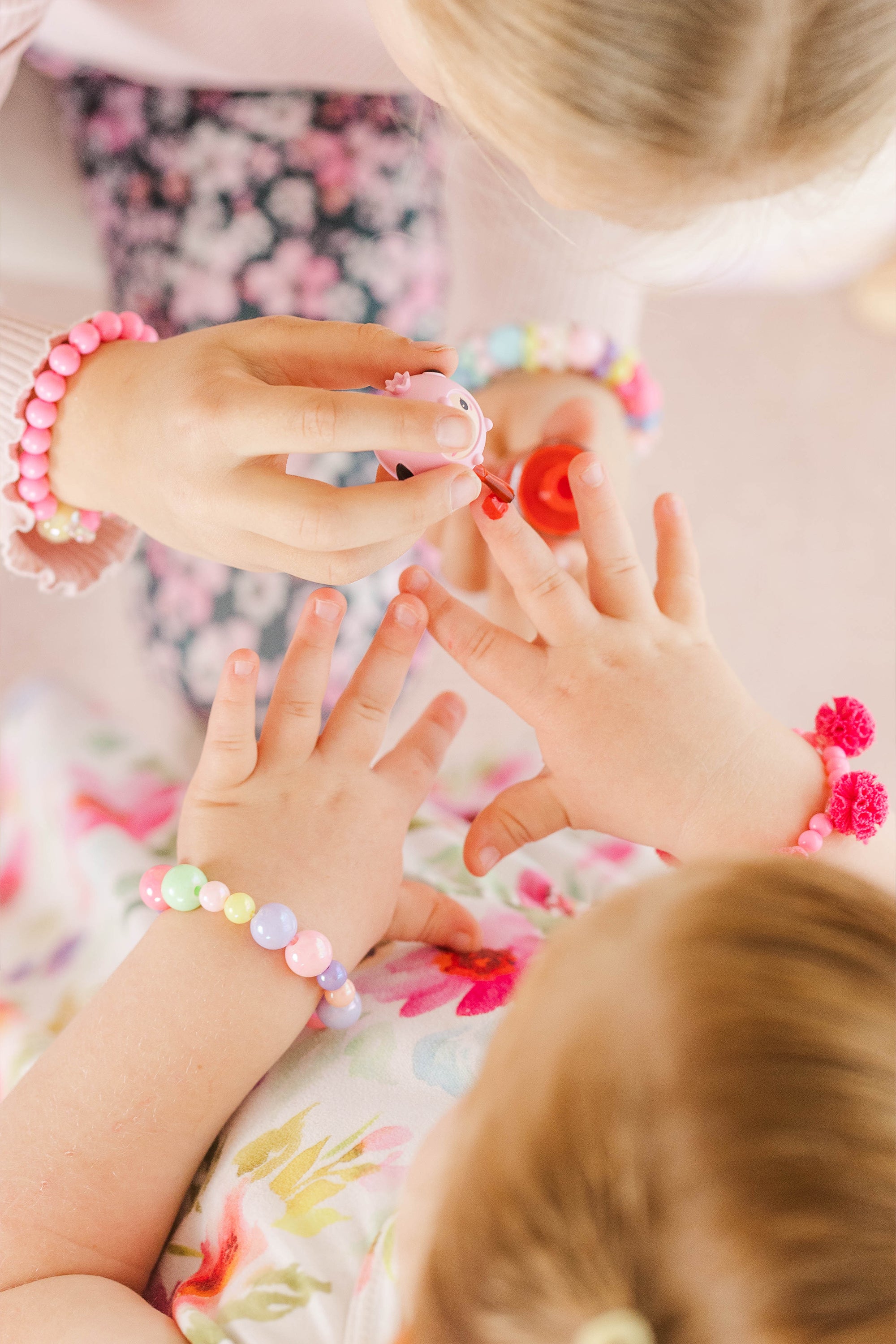 Overhead view of two girls applying nail polish; bracelets, floral print clothing.
