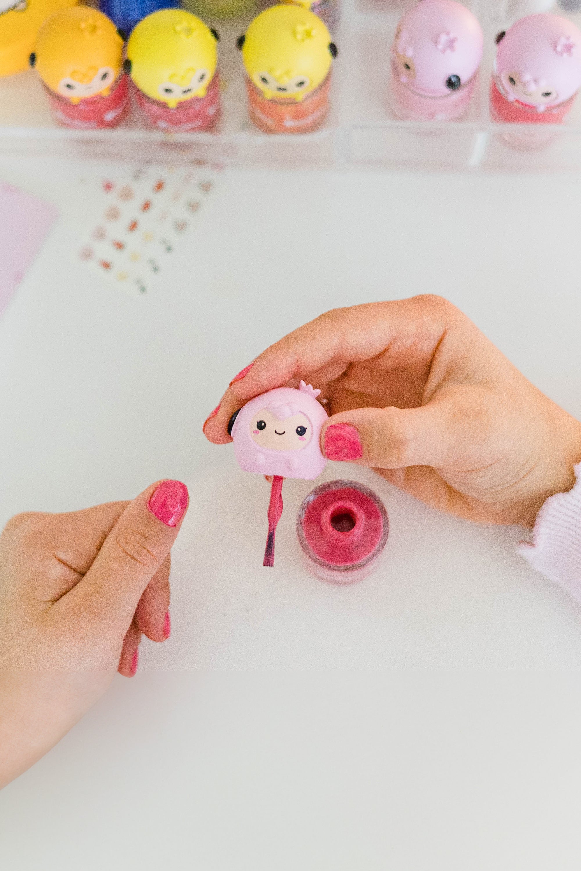 Woman painting nails with pink polish, featuring a cartoon animal-shaped bottle.