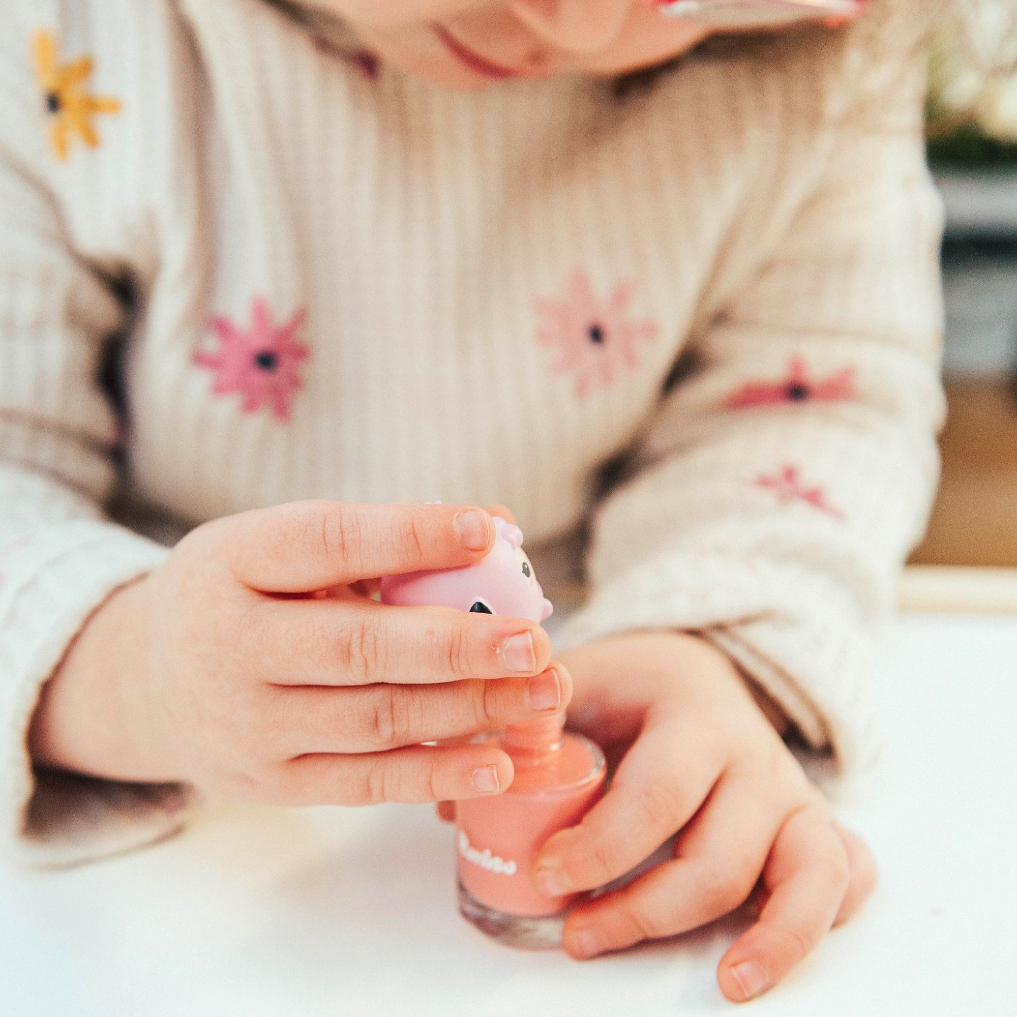 Child in floral sweater holding pink nail polish.