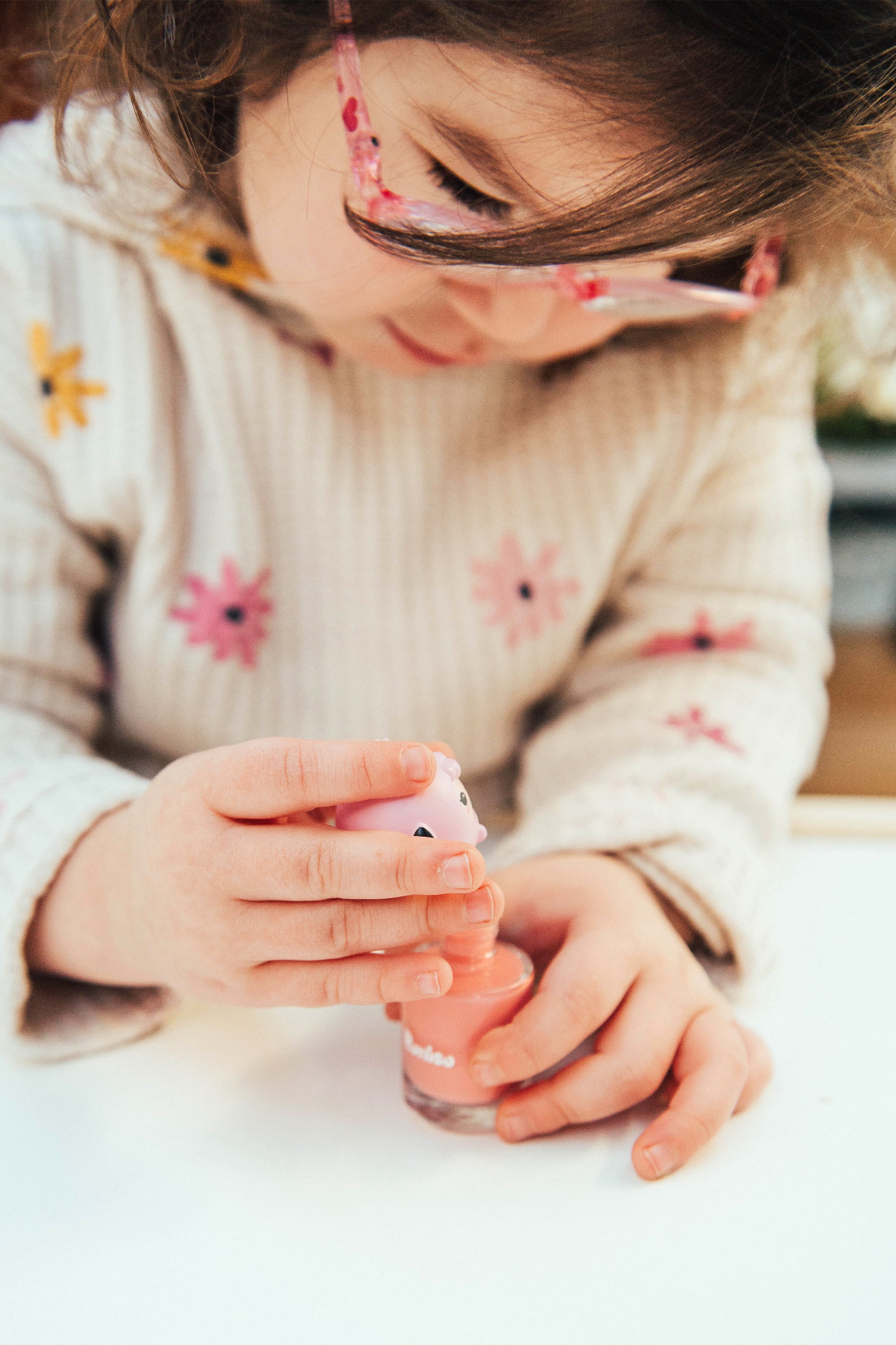 Child with glasses opening pink nail polish bottle.
