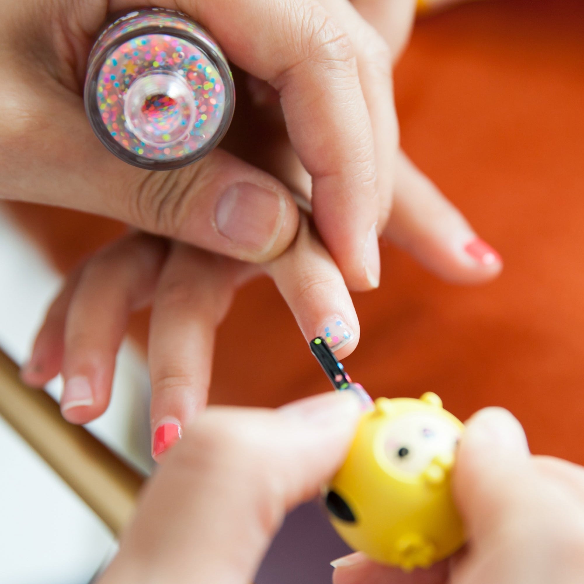 Hands applying glitter nail polish with an owl-shaped bottle.