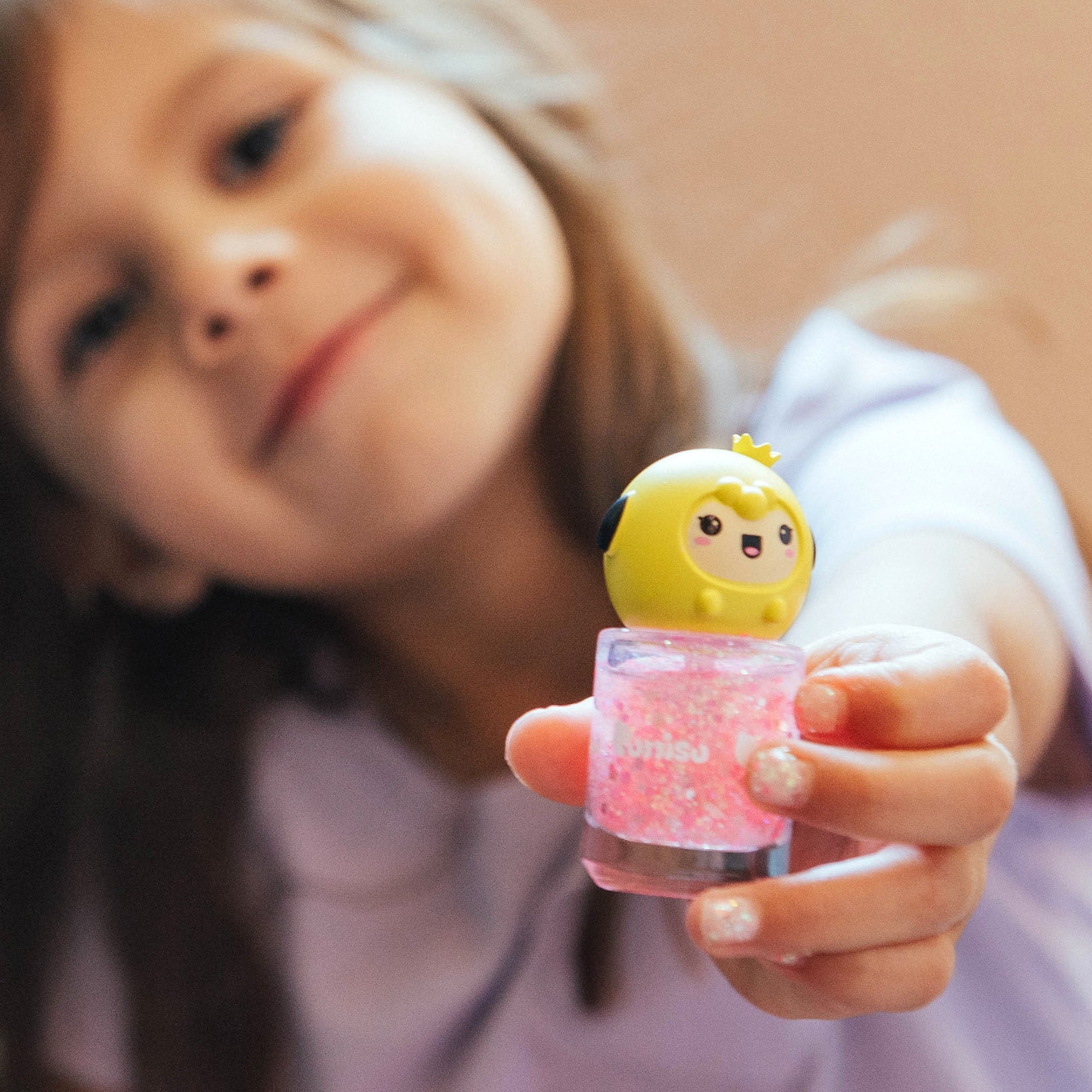 Young girl holds pink glitter nail polish with a cartoon character topper.