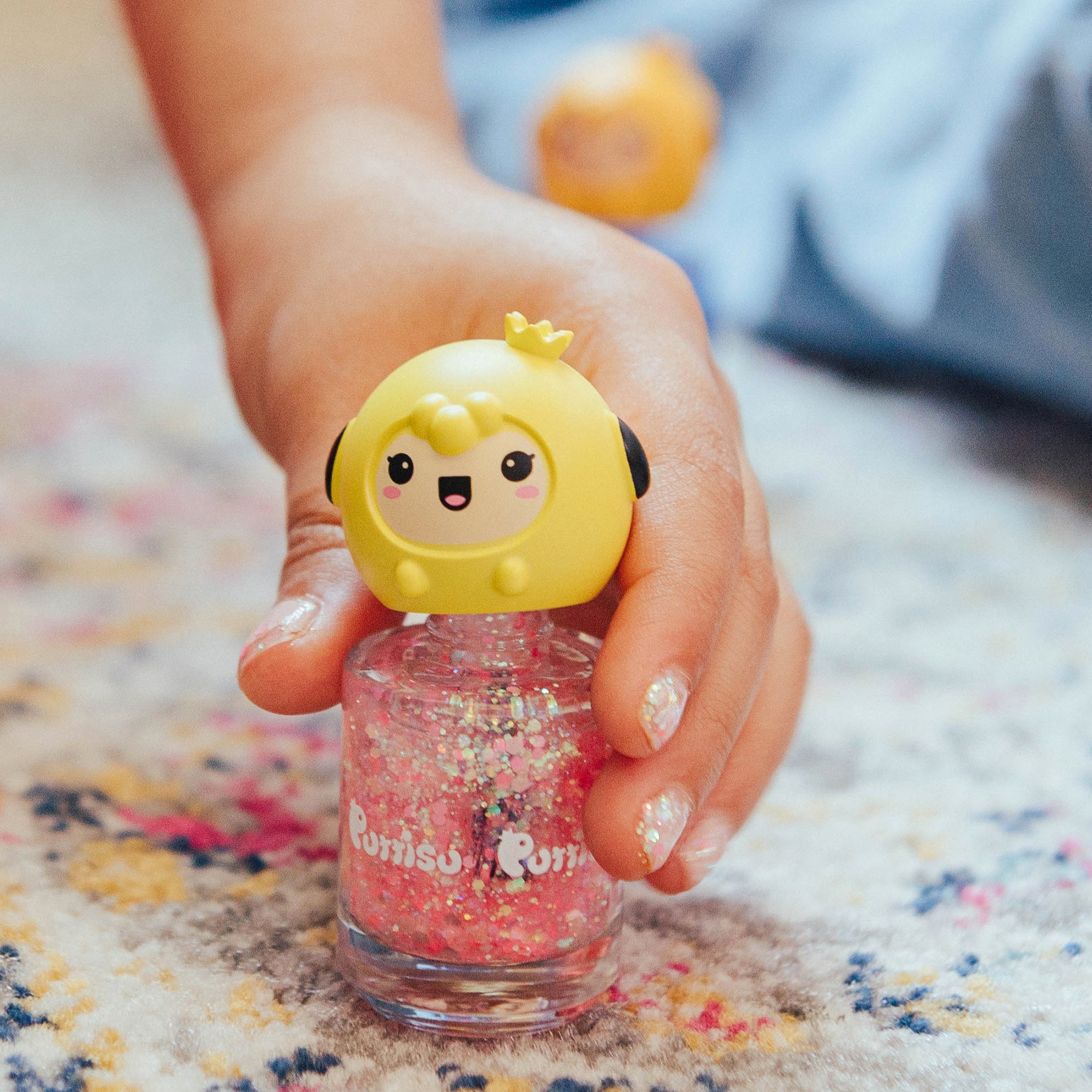 Hand holding pink glittery nail polish with a cartoon character on top.