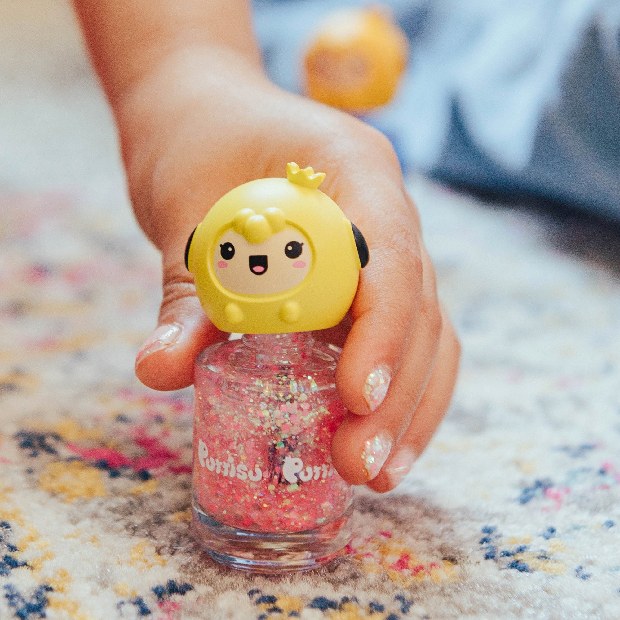 Person holding a bottle of pink glitter nail polish with a yellow cartoon character cap.