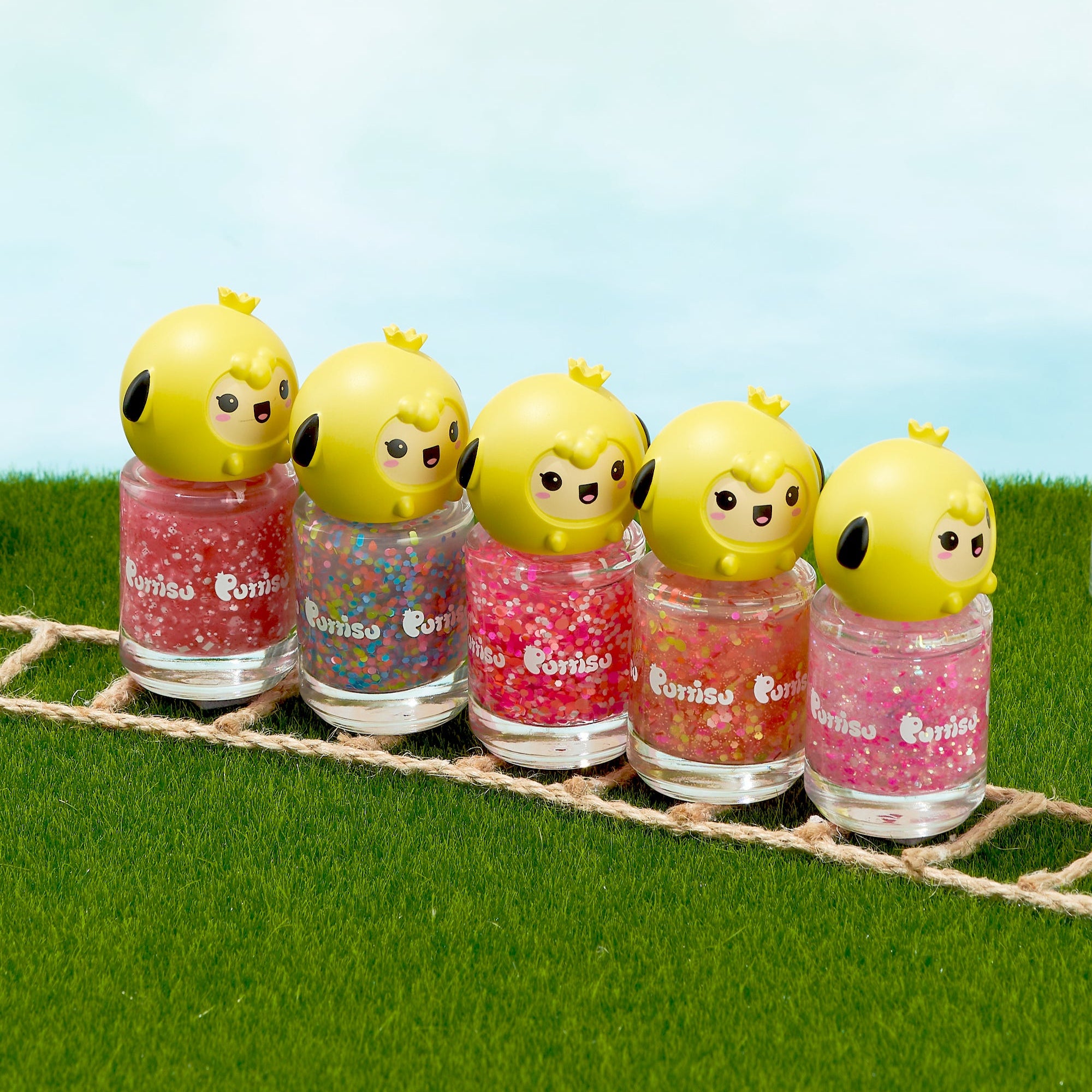 Five nail polish bottles with cartoon chick toppers sit in a row on artificial grass with a rope in front of them.