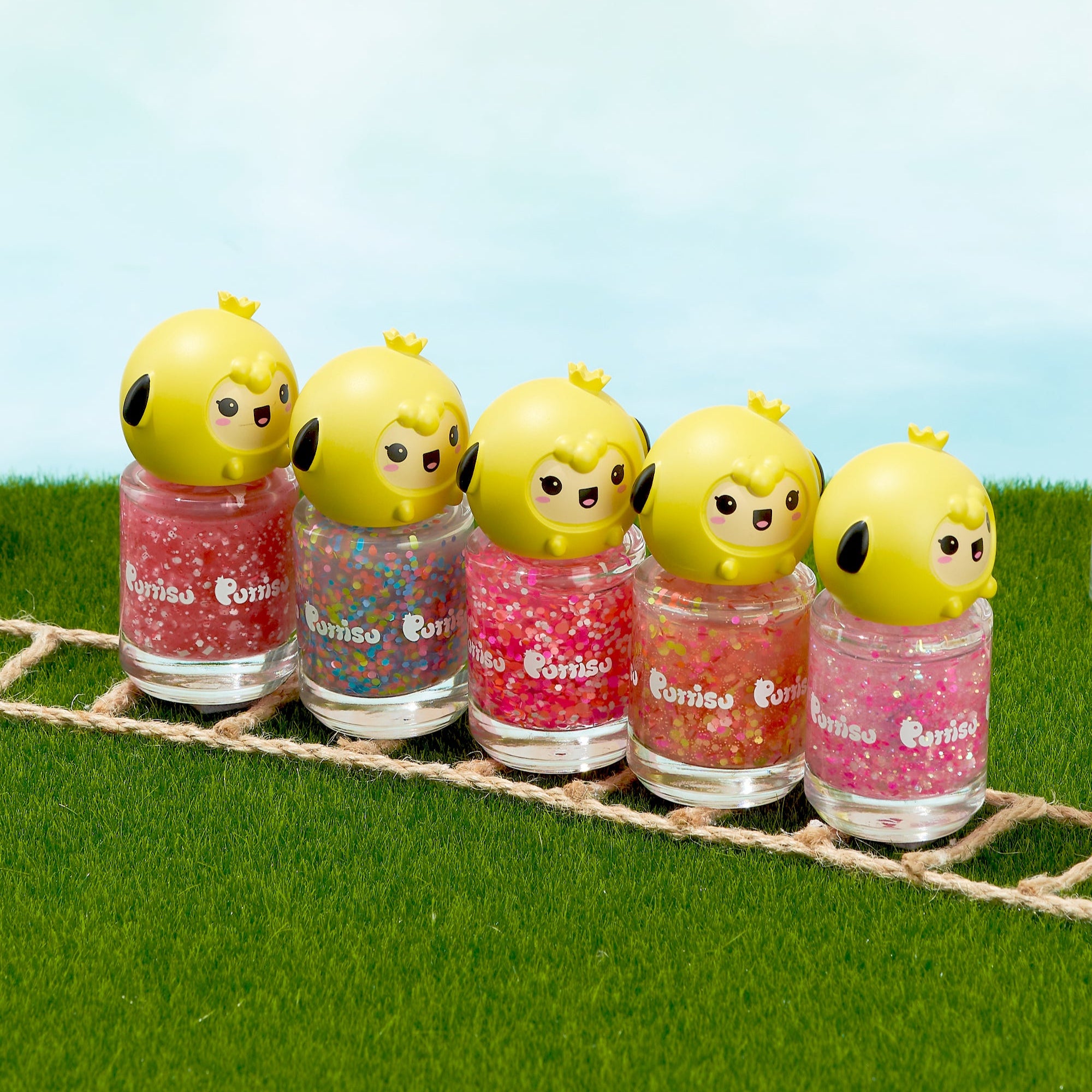 Five nail polish bottles with yellow chick-shaped caps, arranged on green grass.