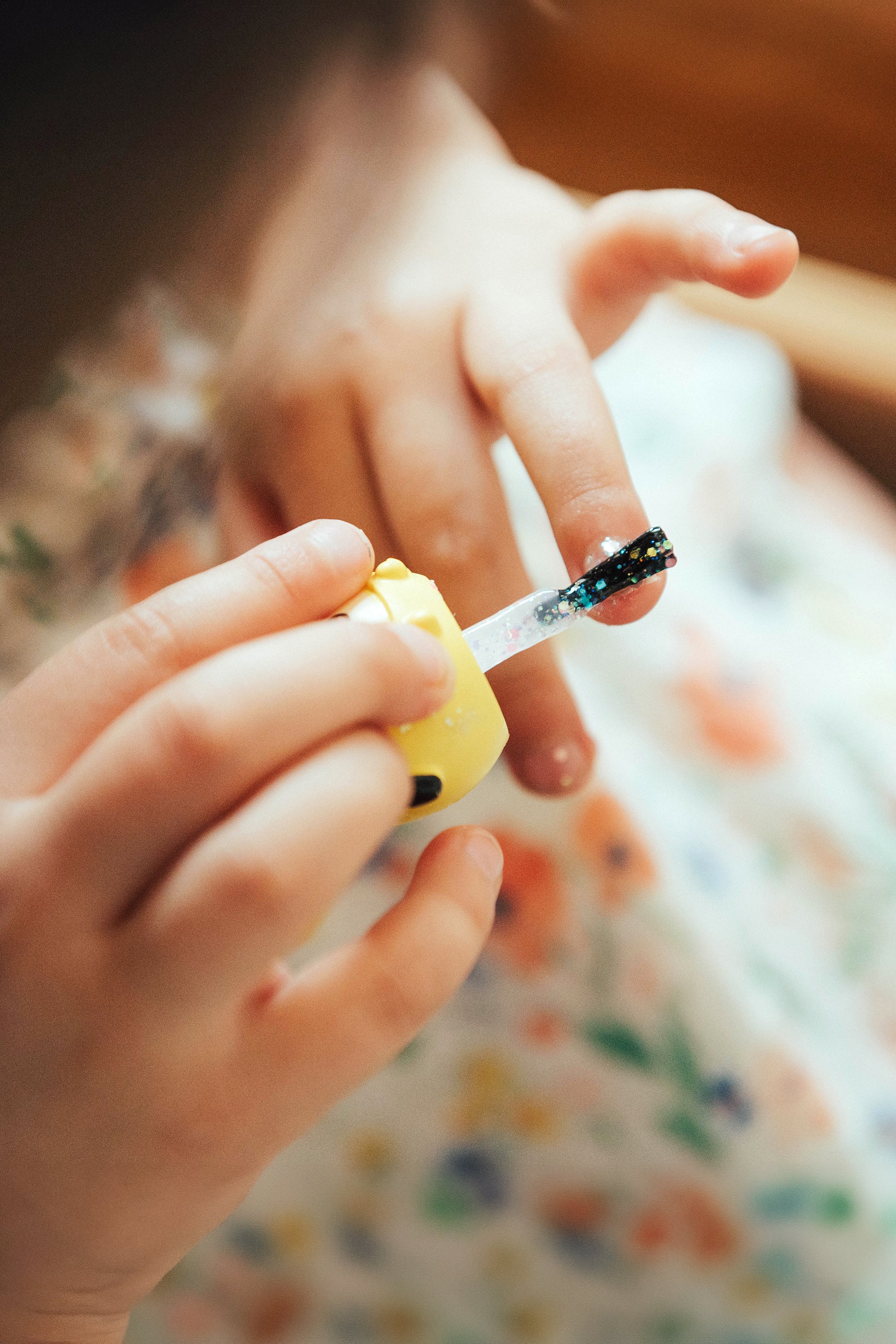 Child applying glittery black nail polish. Floral dress.