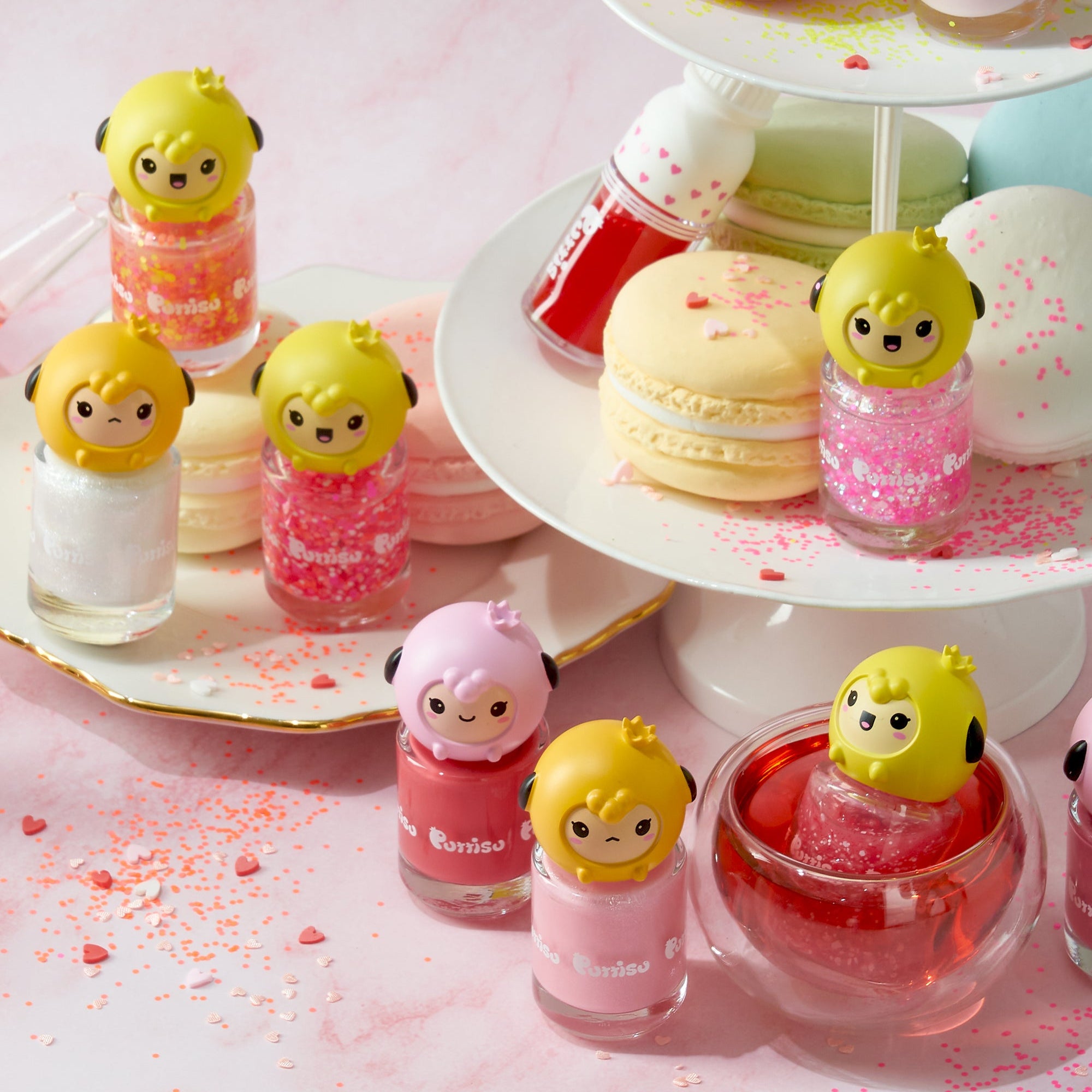 Close-up of colorful, character-topped nail polish bottles and macarons on a pink surface.