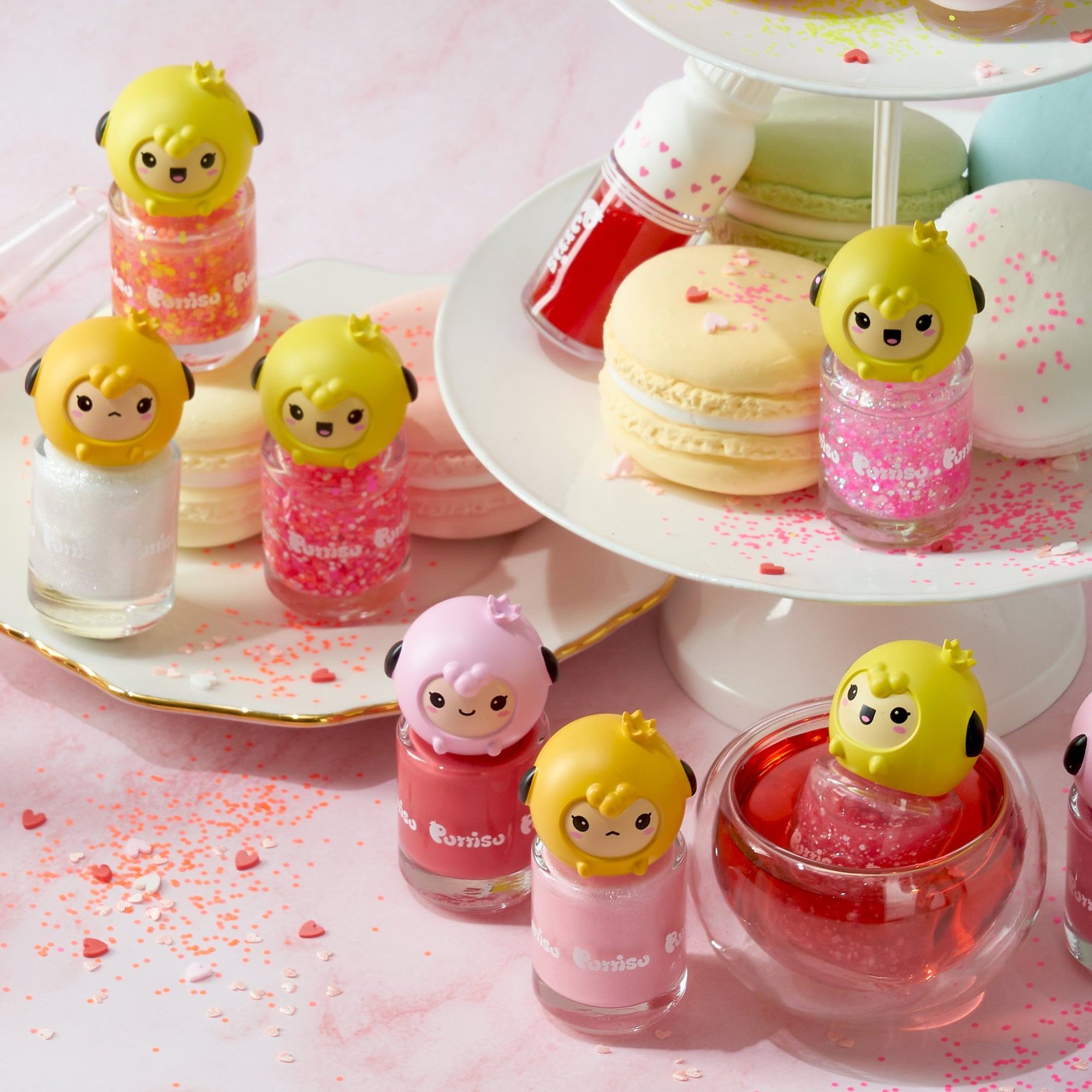 Colorful nail polish bottles with cute cartoon sheep toppers, macarons, and sprinkles on a pink surface.