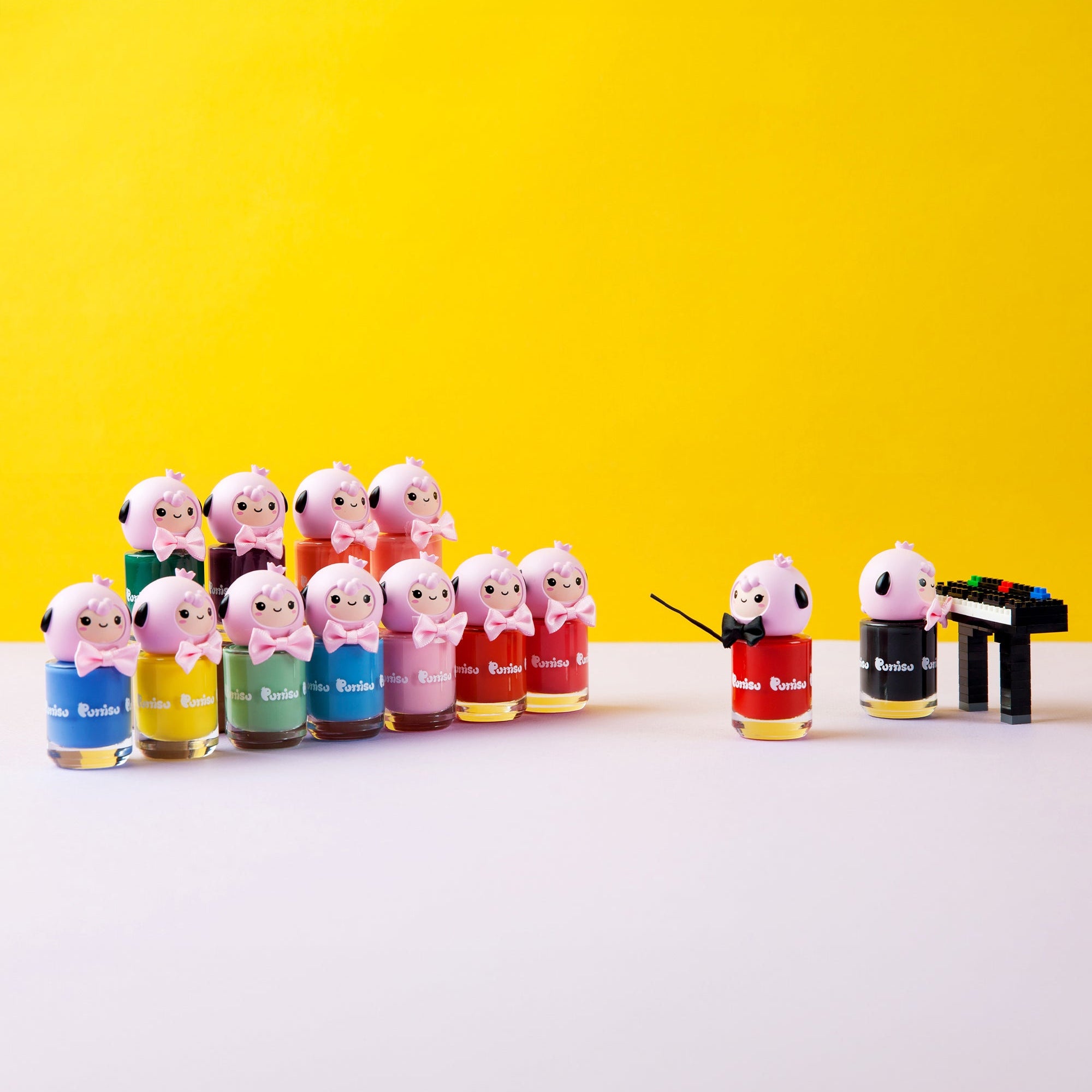 Product image of a choir made of 13 nail polish bottles with lamb-like bottle caps wearing bowties, one holding a conductor's baton, and a piano made of Lego-like blocks.