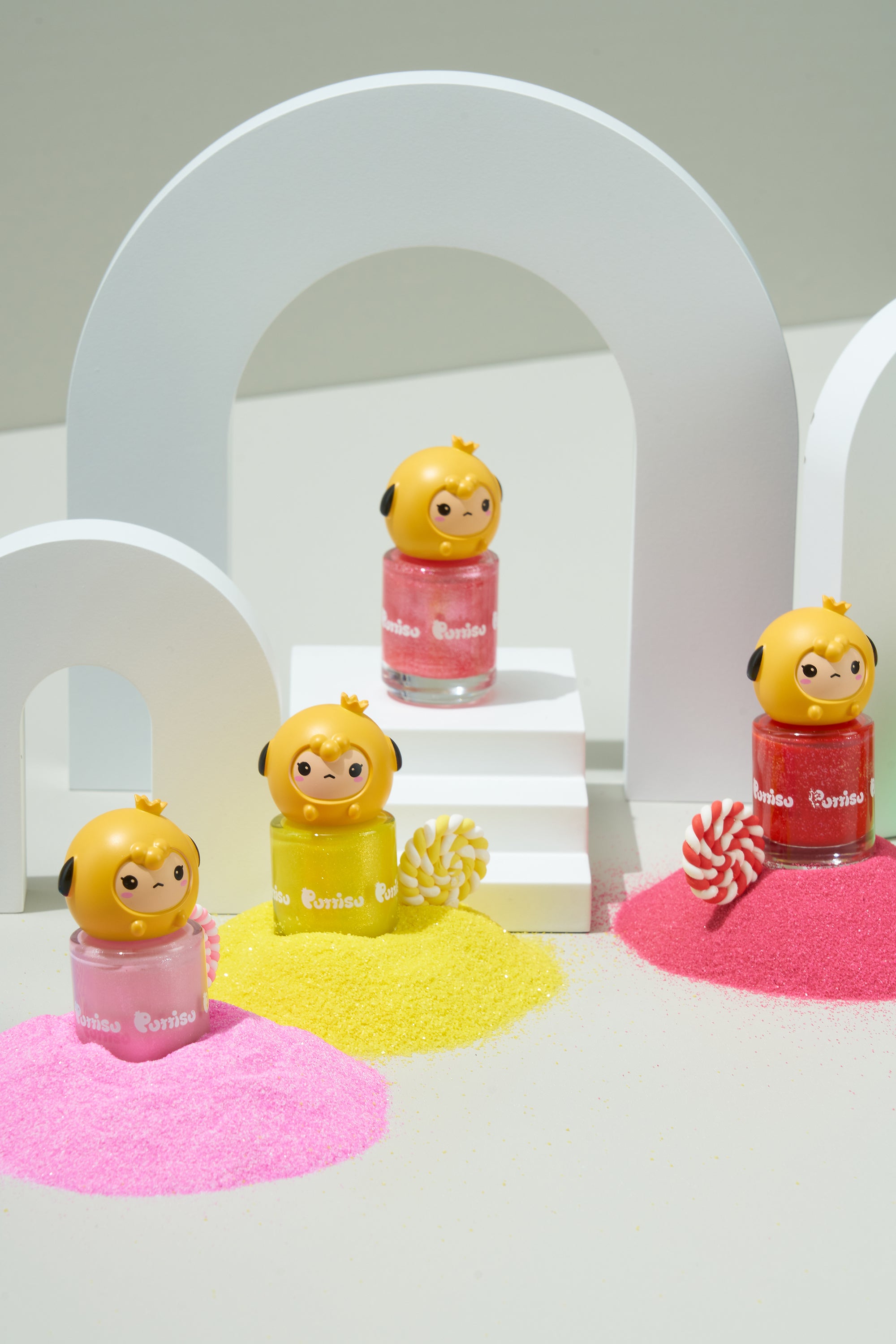Three bottles of colorful glitter nail polish with character toppers, arranged with matching glitter sand and white arches.