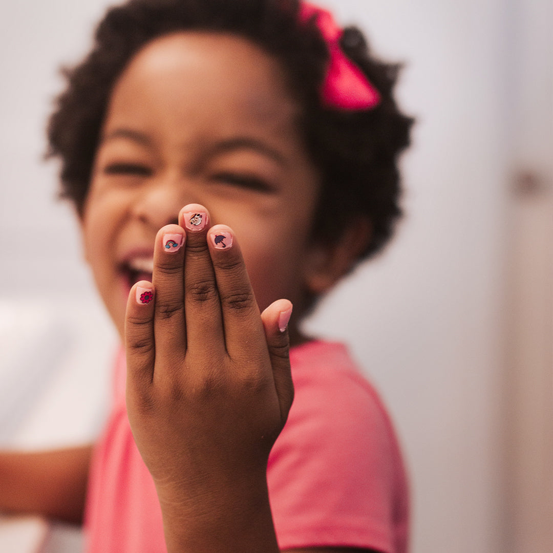 A smiling girl holding up her hand with nail art stickers.