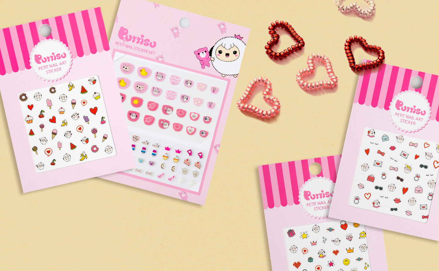Puttisu Petit Nail Art Sticker sets in pink packaging featuring cute designs like hearts, animals, and sweets, displayed with heart-shaped accessories on a beige background.