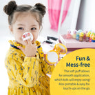 A young girl with two buns in her hair applies makeup with a yellow compact and white puff on her nose, wearing a patterned yellow dress in front of a pink vanity with nail polish bottles. A text overlay says, "Fun & Mess-free" with a product description.
