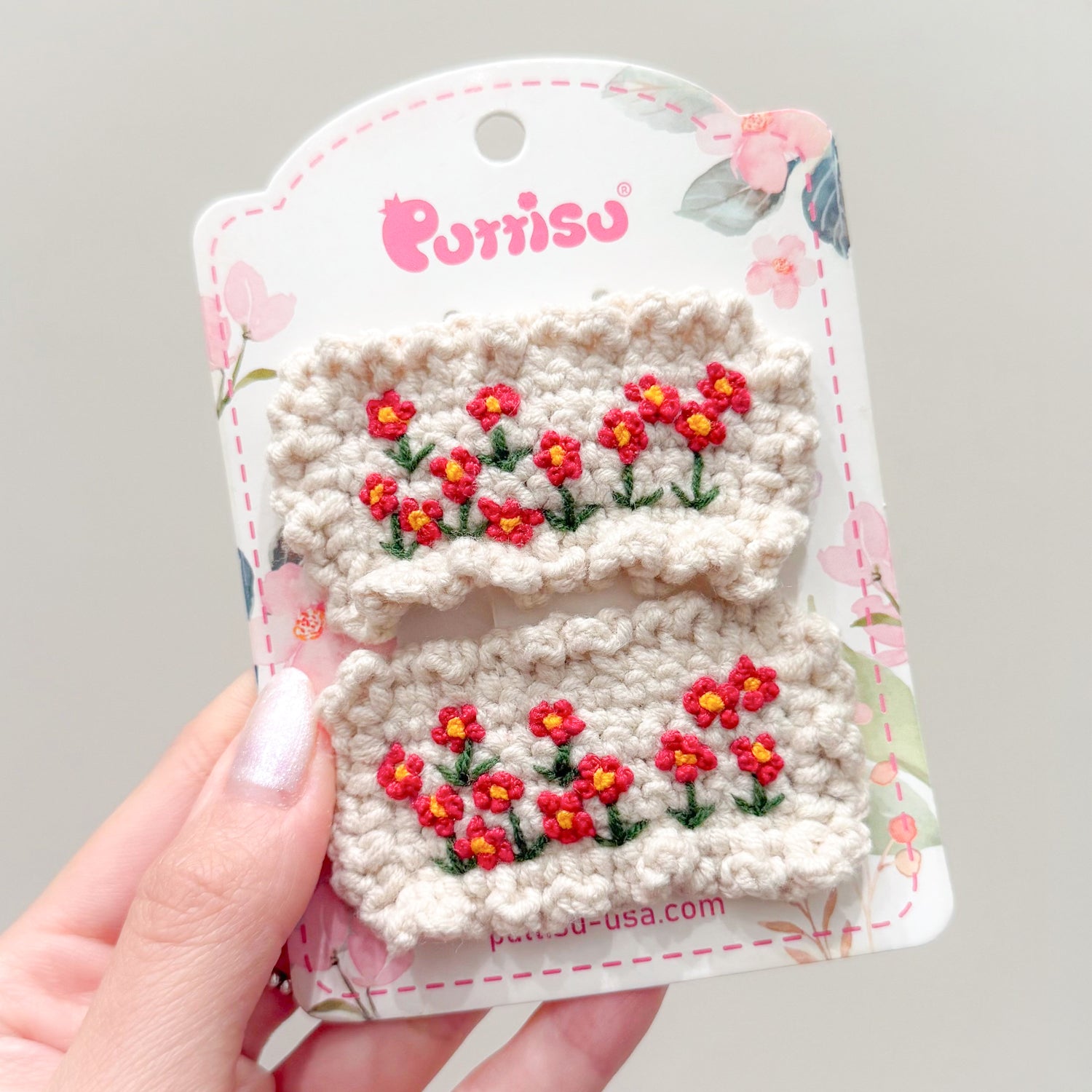 Two crochet hair clips with red flowers on a floral-patterned card.