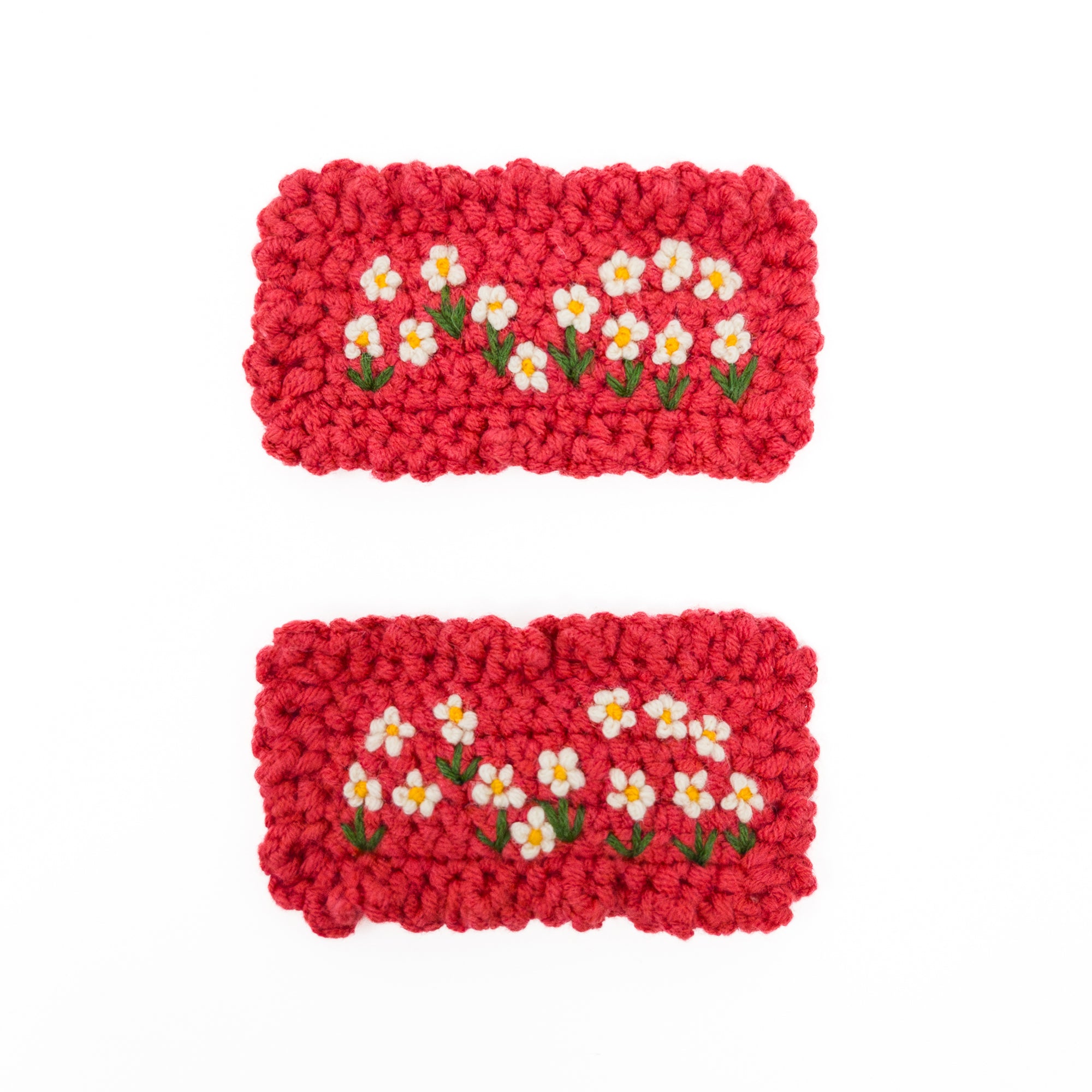 Two red crocheted fabric rectangles with embroidered daisy designs.