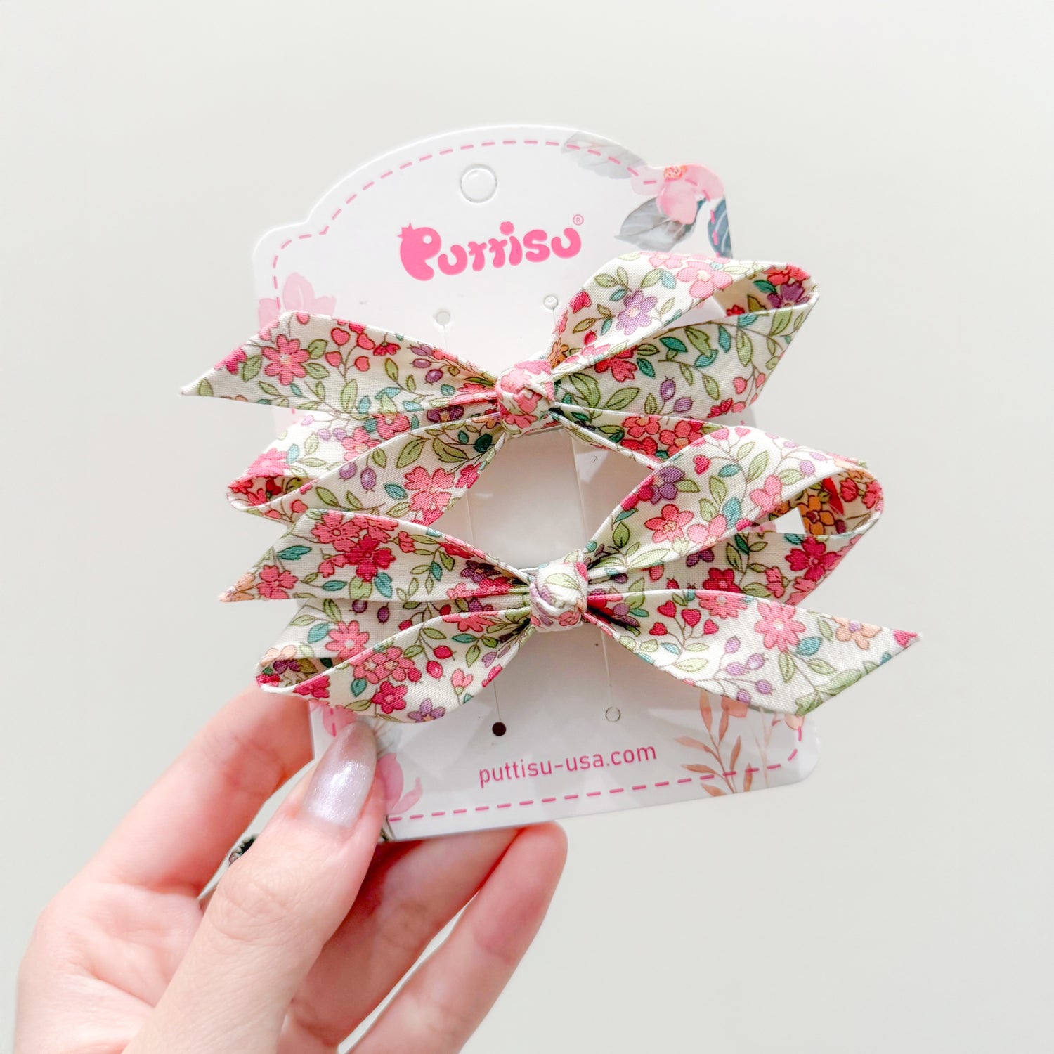 Two floral hair bows on a white display card held by a hand.