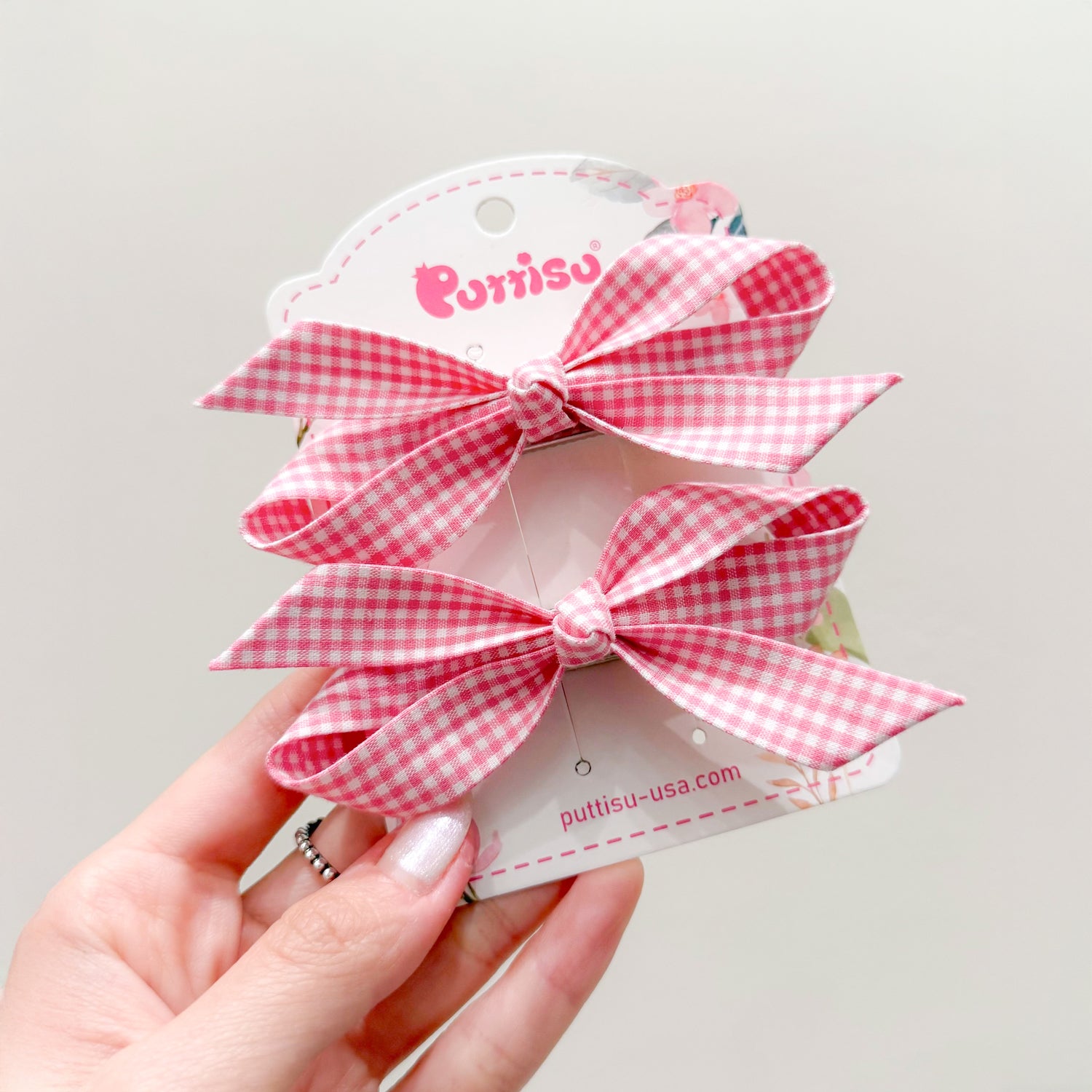 Two pink gingham hair bows on a white brand card, held in a hand.